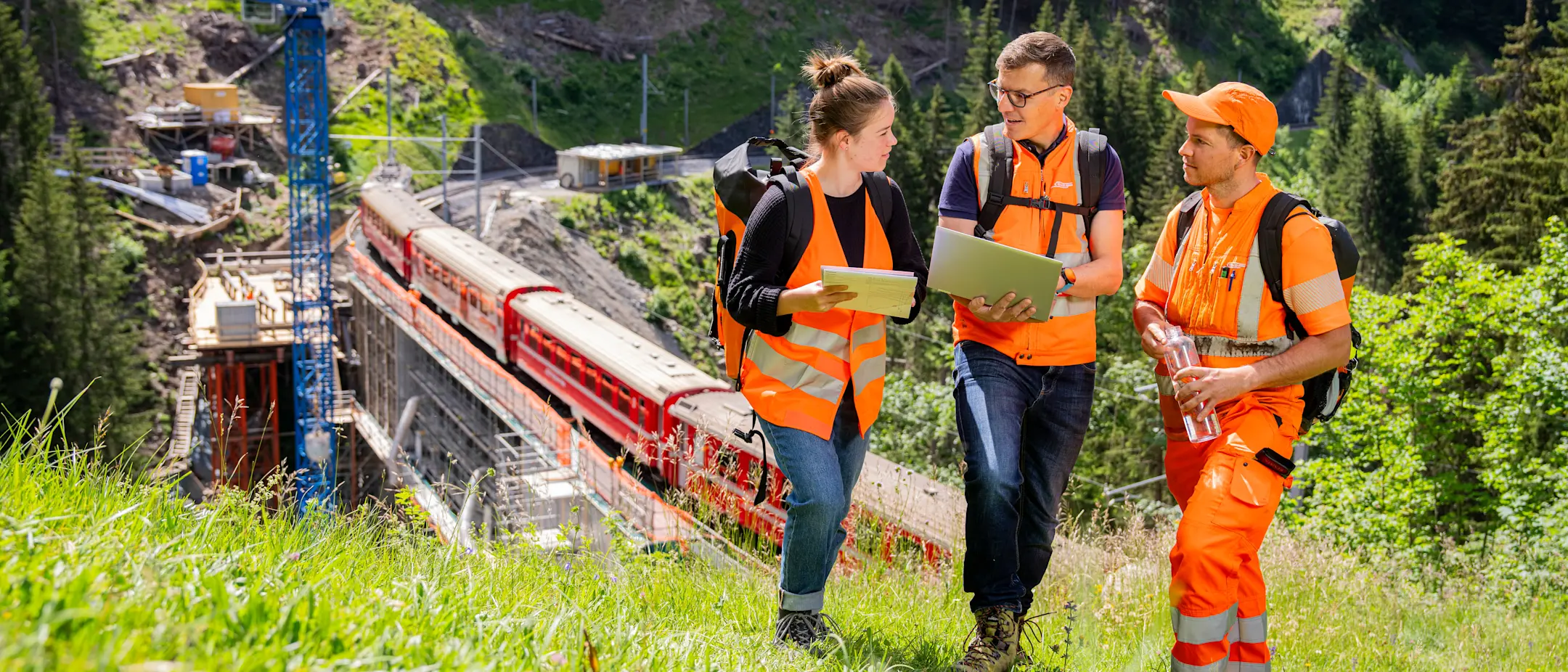 Eine Ingenieurin, ein Auditor und ein Gleisbauer im Gespräch oberhalb einer Baustelle
