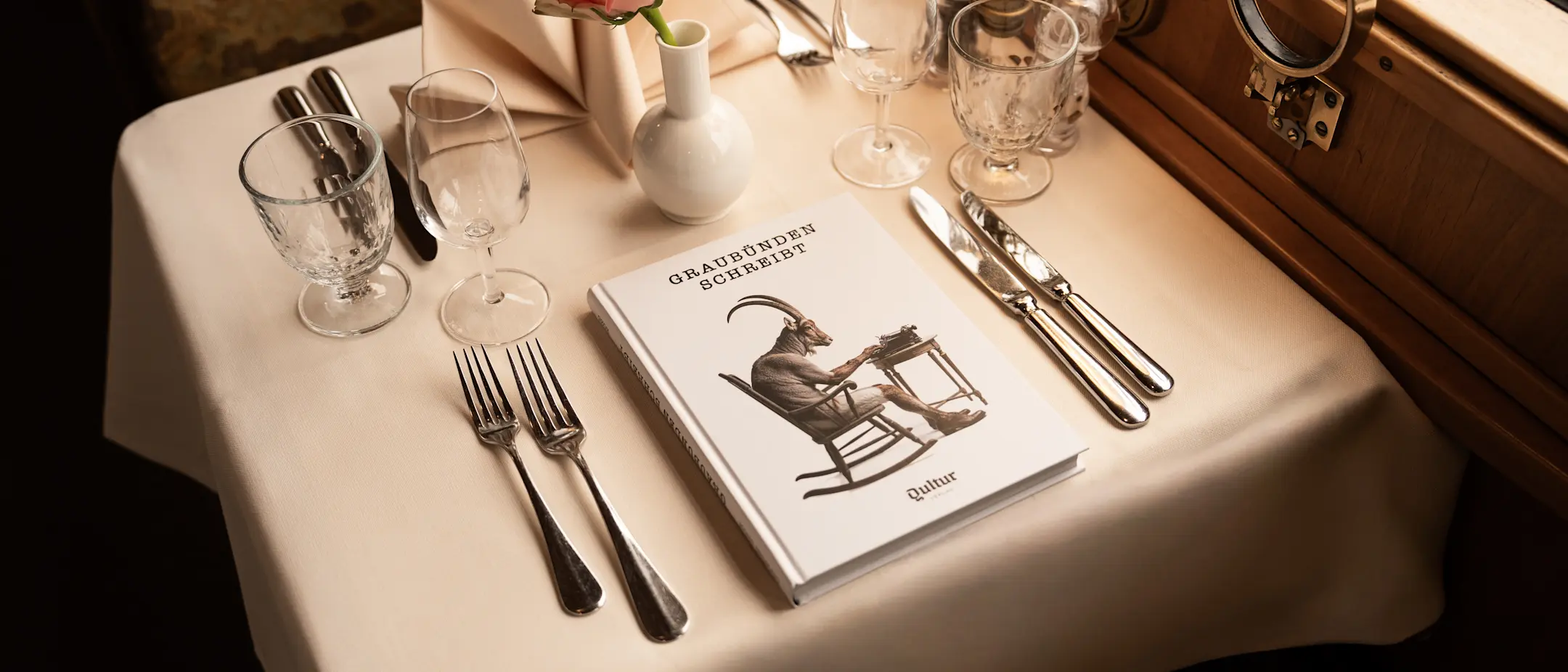 Auf dem gedeckten Tisch im Speisewagen Gourmino liegt das Buch «Graubünden schreibt» anstelle eines Tellers.