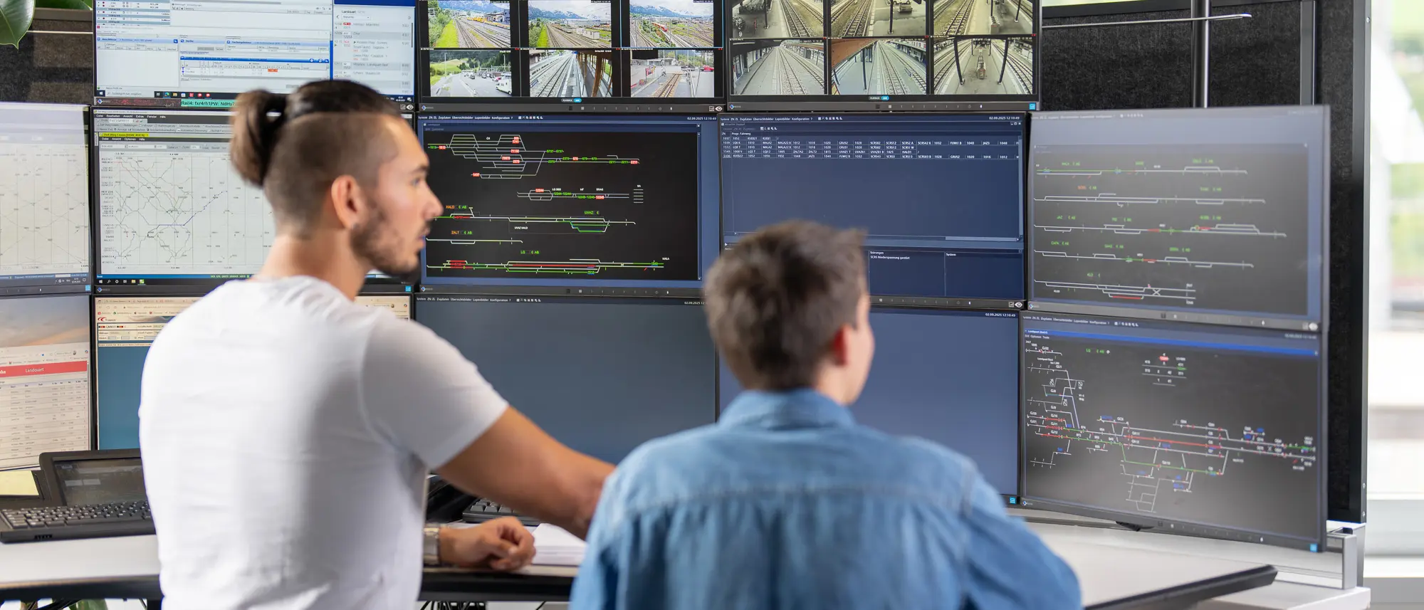 Zugverkehrsleiter mit Lernender bei der Arbeit mit Blick auf viele Bildschirme