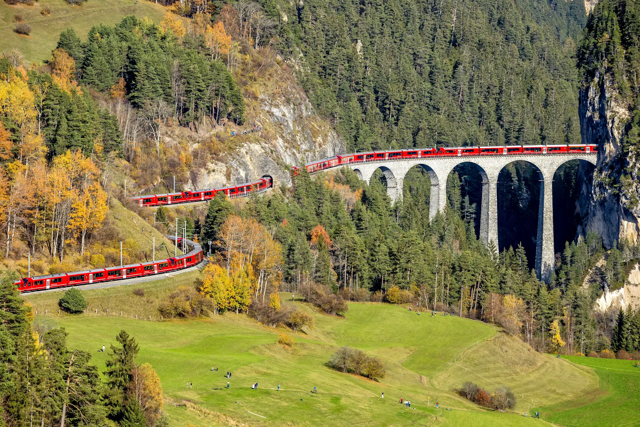 Ein über 1,9 km langer roter Zug der RhB schlängelt sich über das Landwasserviadukt inmitten einer Gebirgslandschaft.