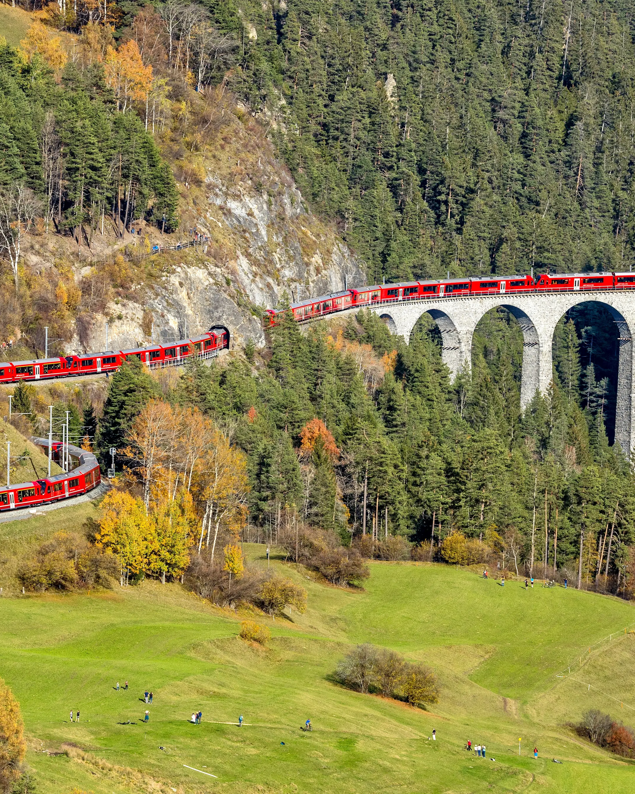 Ein über 1,9 km langer roter Zug der RhB schlängelt sich über das Landwasserviadukt inmitten einer Gebirgslandschaft.