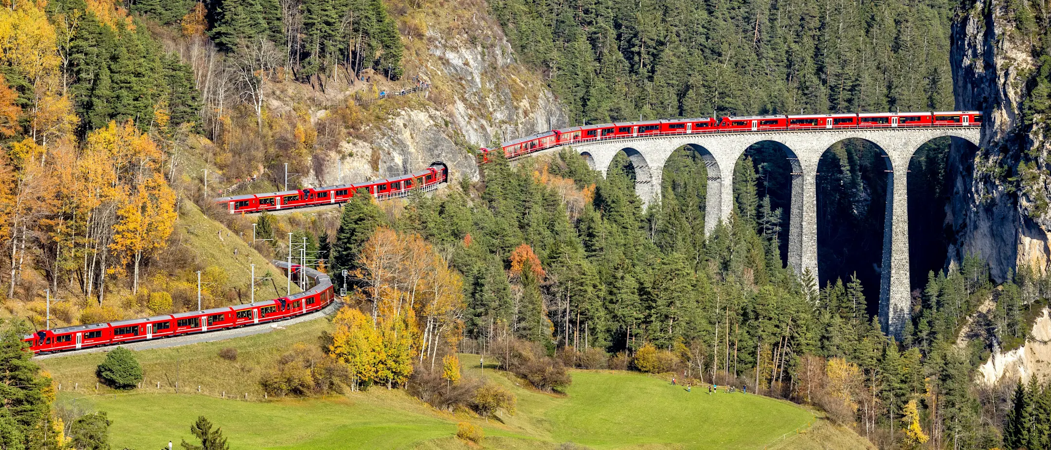 Ein über 1,9 km langer roter Zug der RhB schlängelt sich über das Landwasserviadukt inmitten einer Gebirgslandschaft.
