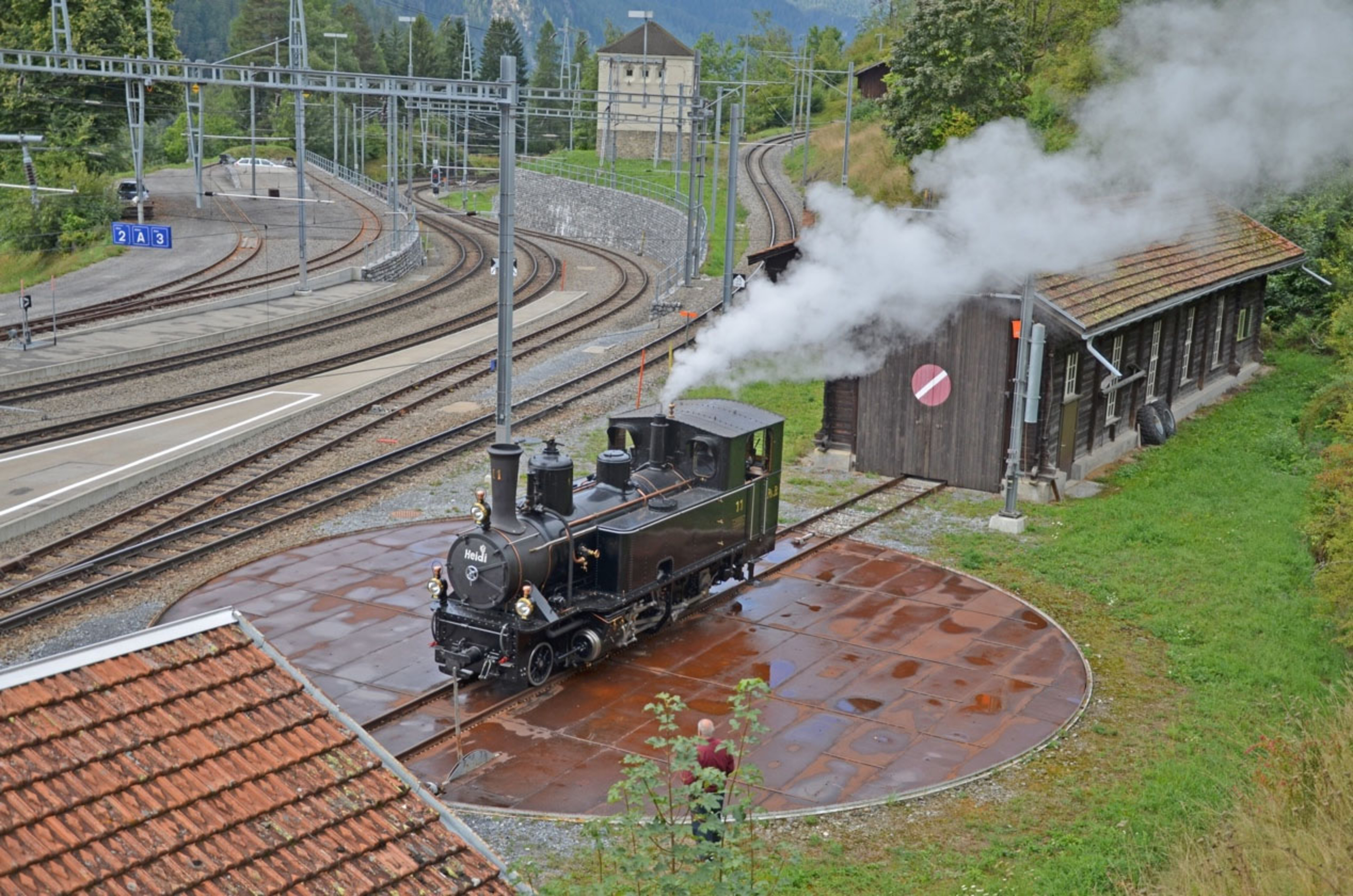 Die Dampflokomotive Heidi steht vor einem alten Bahnhof. 