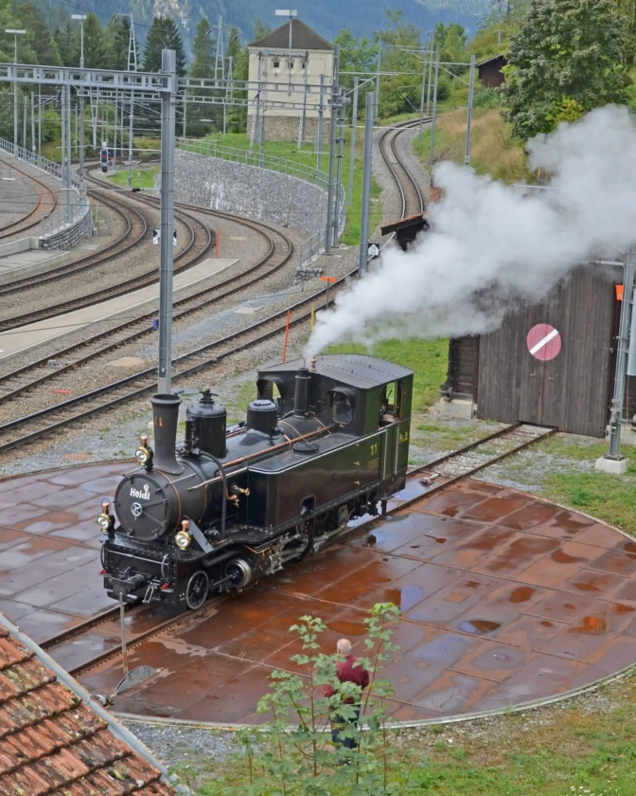 Die Dampflokomotive Heidi steht vor einem alten Bahnhof.