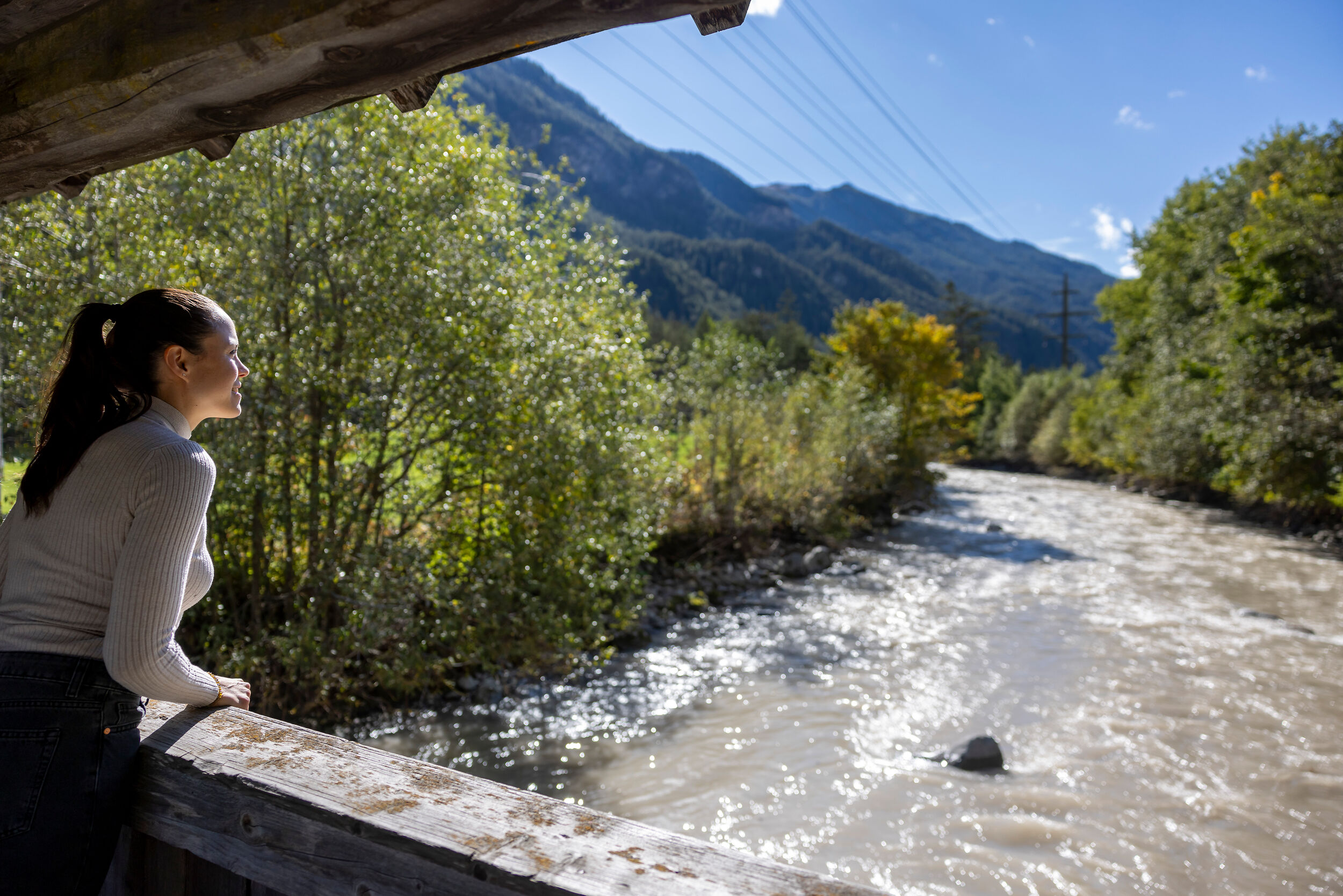 Eine Frau steht auf einer Brücke und schaut in Richtung Fluss.