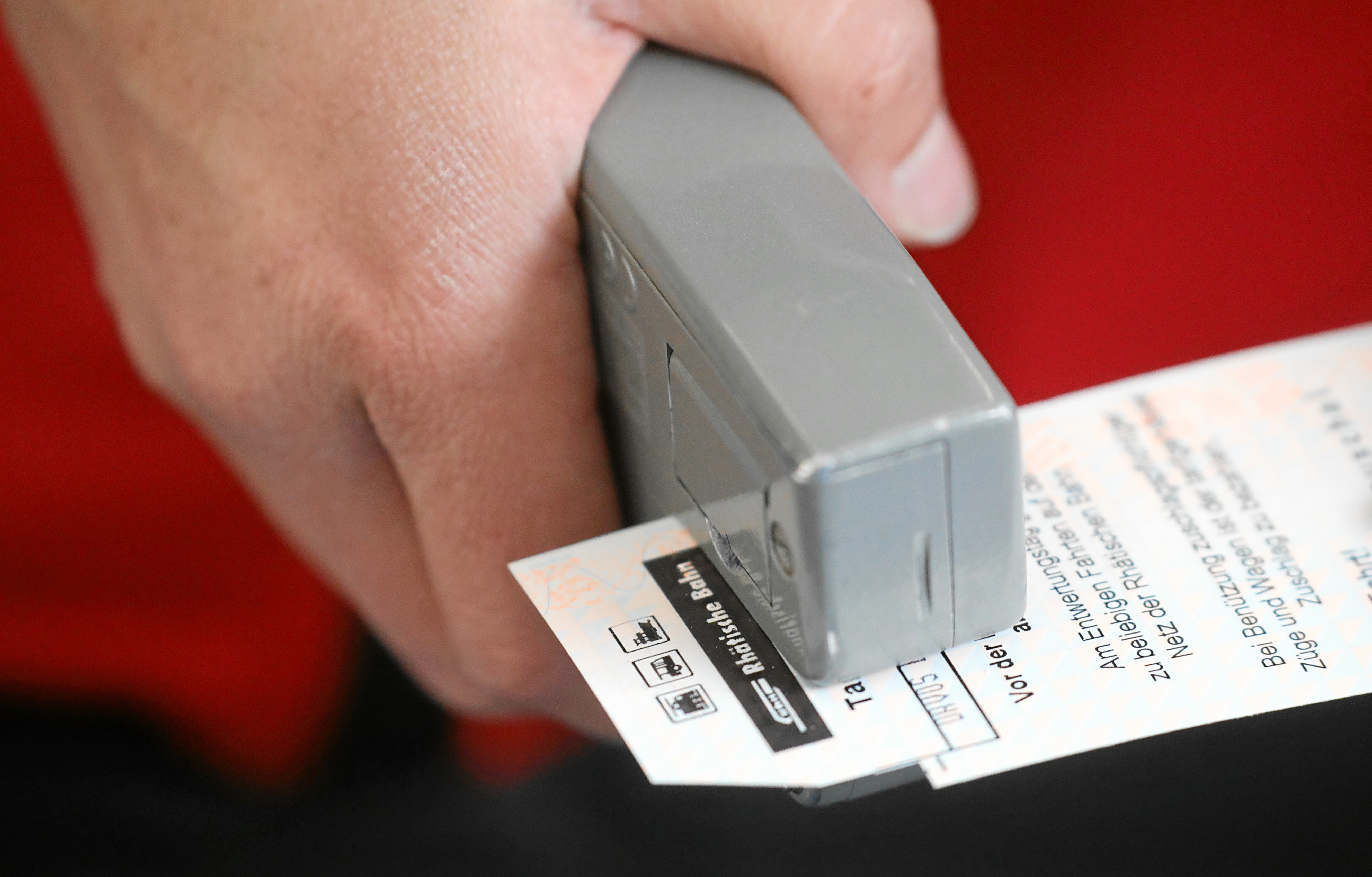 Primo piano di una mano che timbra un biglietto della Ferrovia retica con una obliteratrice.