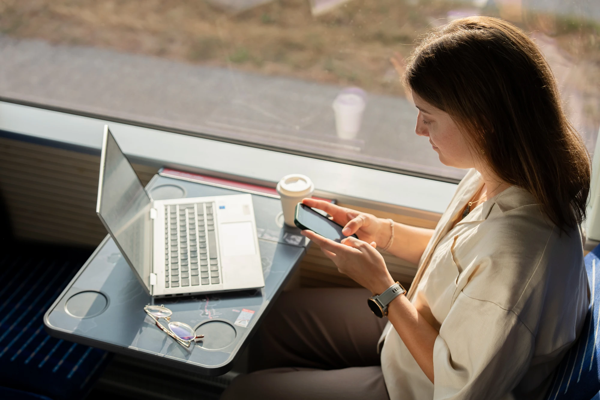Eine Mitarbeiterin sitzt im Zug mit Laptop und Handy