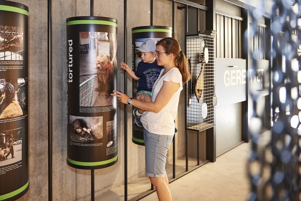 Eine Mutter zeigt ihrem Kind eine Ausstellungstafel im Arosa Bärenland, die über das Leid misshandelter Bären informiert.