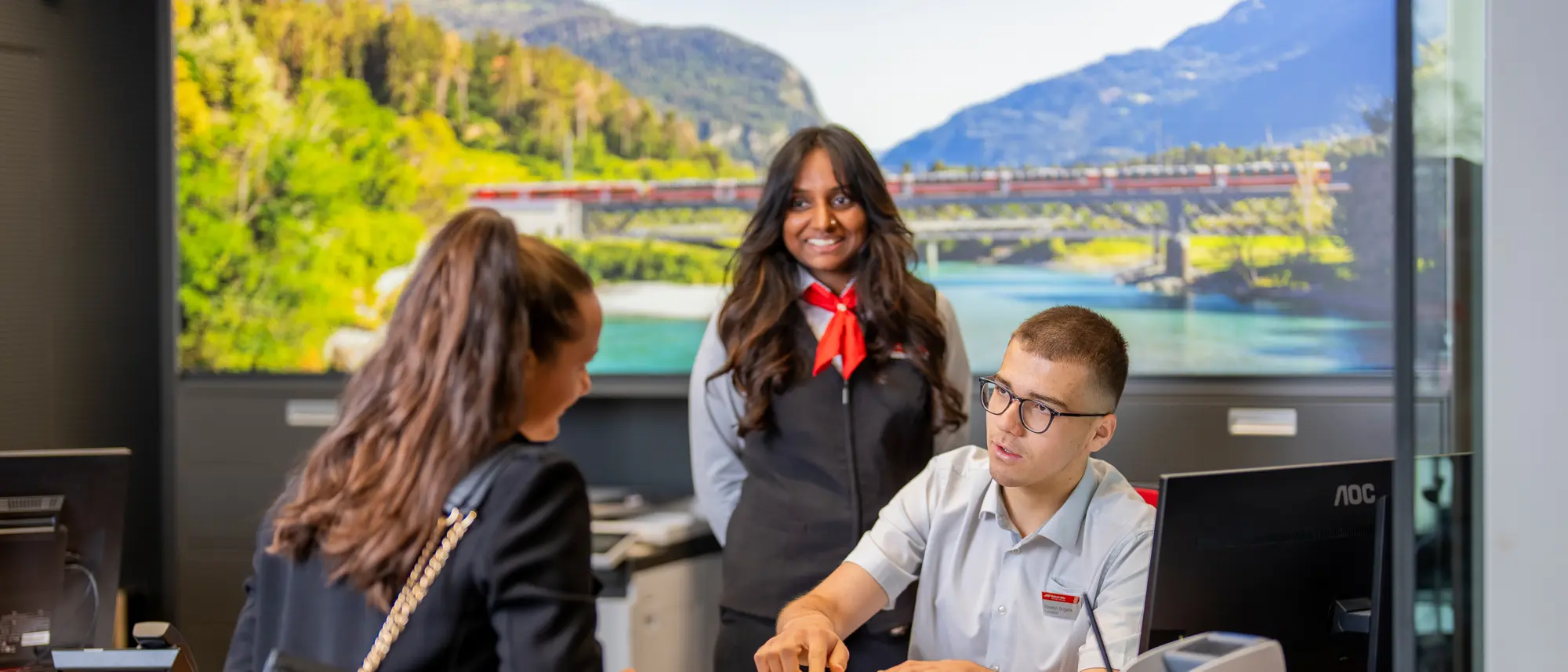 Eine RhB-Mitarbeiterin und ein RhB-Mitarbeiter während einer Besprechung vor einem Computerbildschirm im Büro.