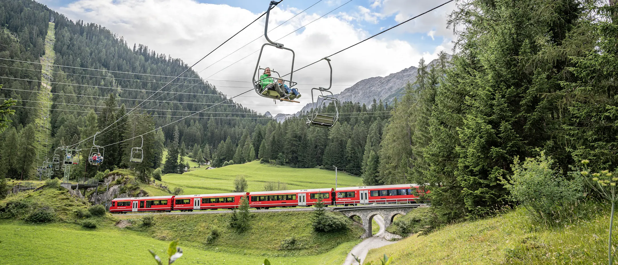 Die Sesselbahn Darlux als Teil der Erlebniswelt Wald der Landwasserwelten, im Hintergrund ein Regio der RhB