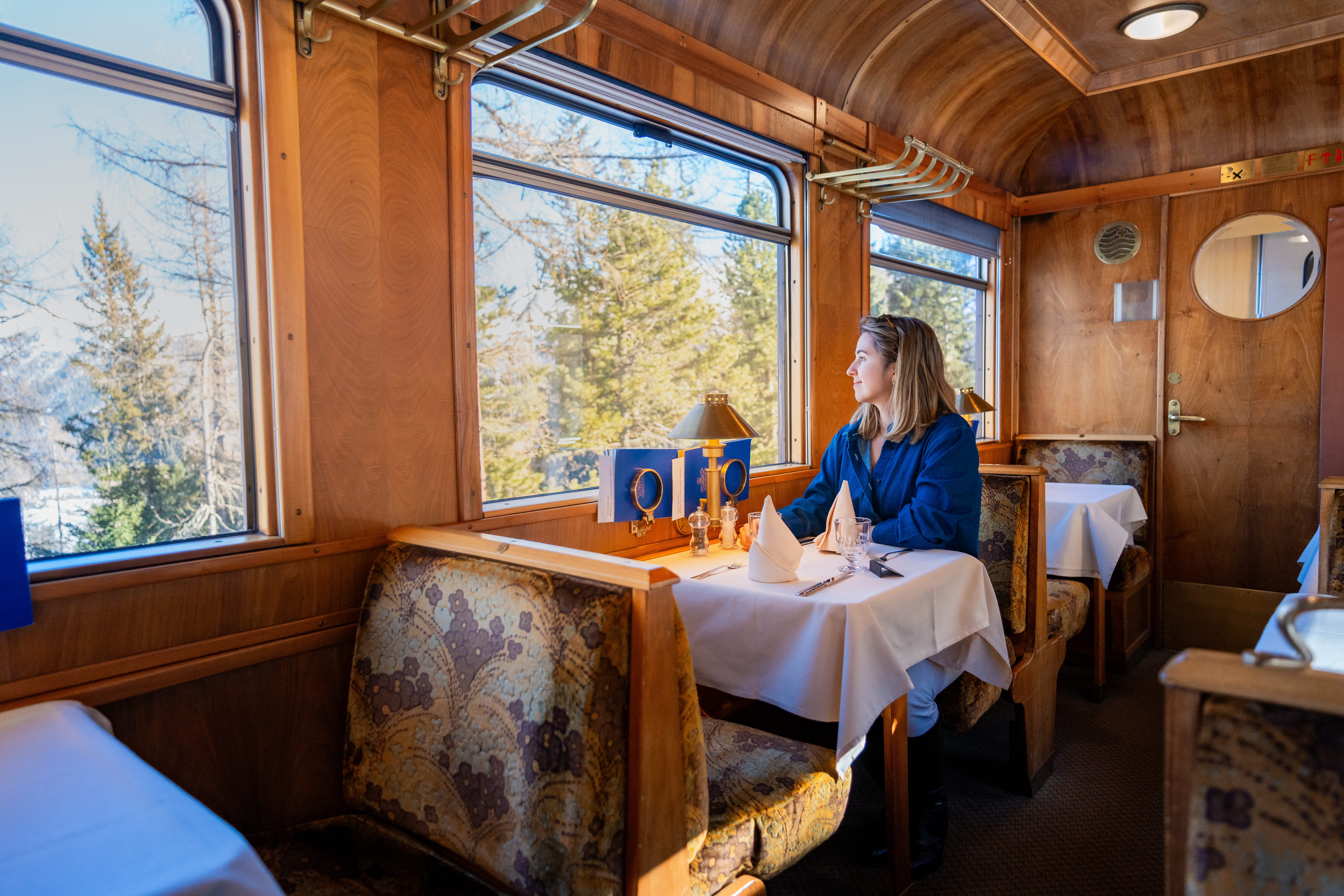 Frau sitzt an einem weiß gedeckten Tisch im historischen Speisewagen Gourmino und genießt die Aussicht durch das Zugfenster.