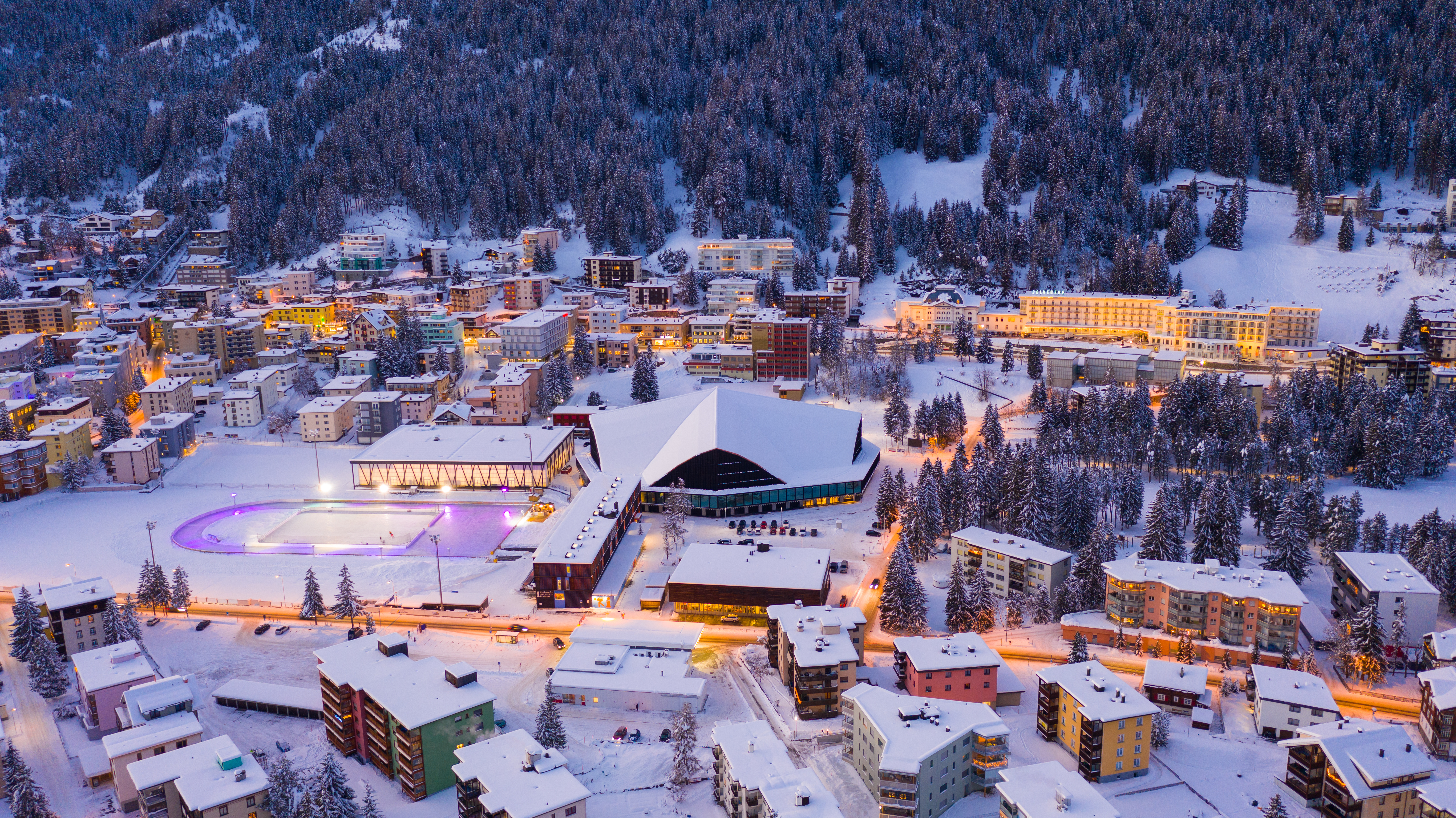 Panoramaansicht auf Davos mit dem Eisfeld und dem Eishockeystadion im Abendlicht. 