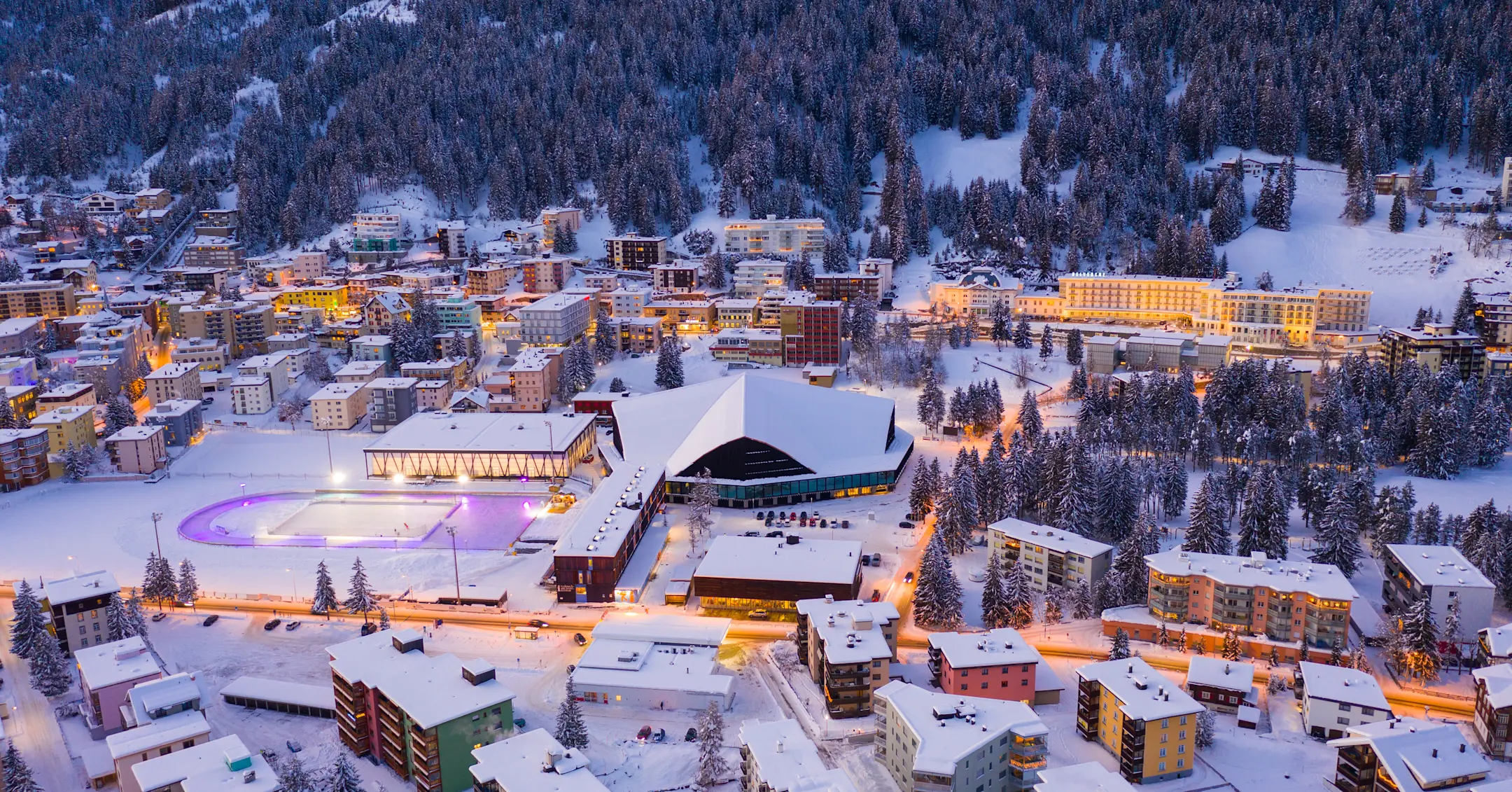 Panoramaansicht auf Davos mit dem Eisfeld und dem Eishockeystadion im Abendlicht.
