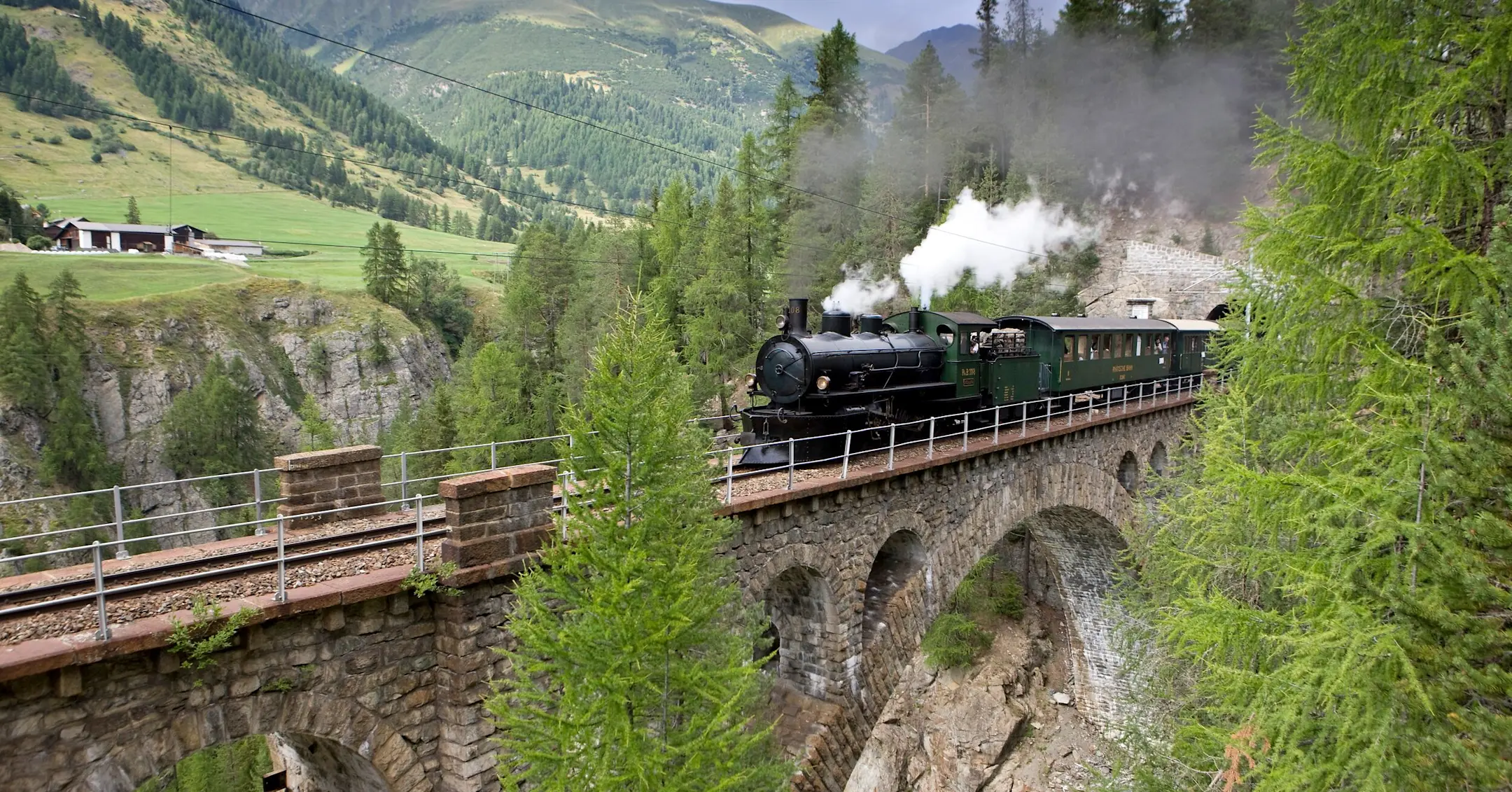 Ein Dampfzug der RhB fährt über ein Viadukt im Engadin.