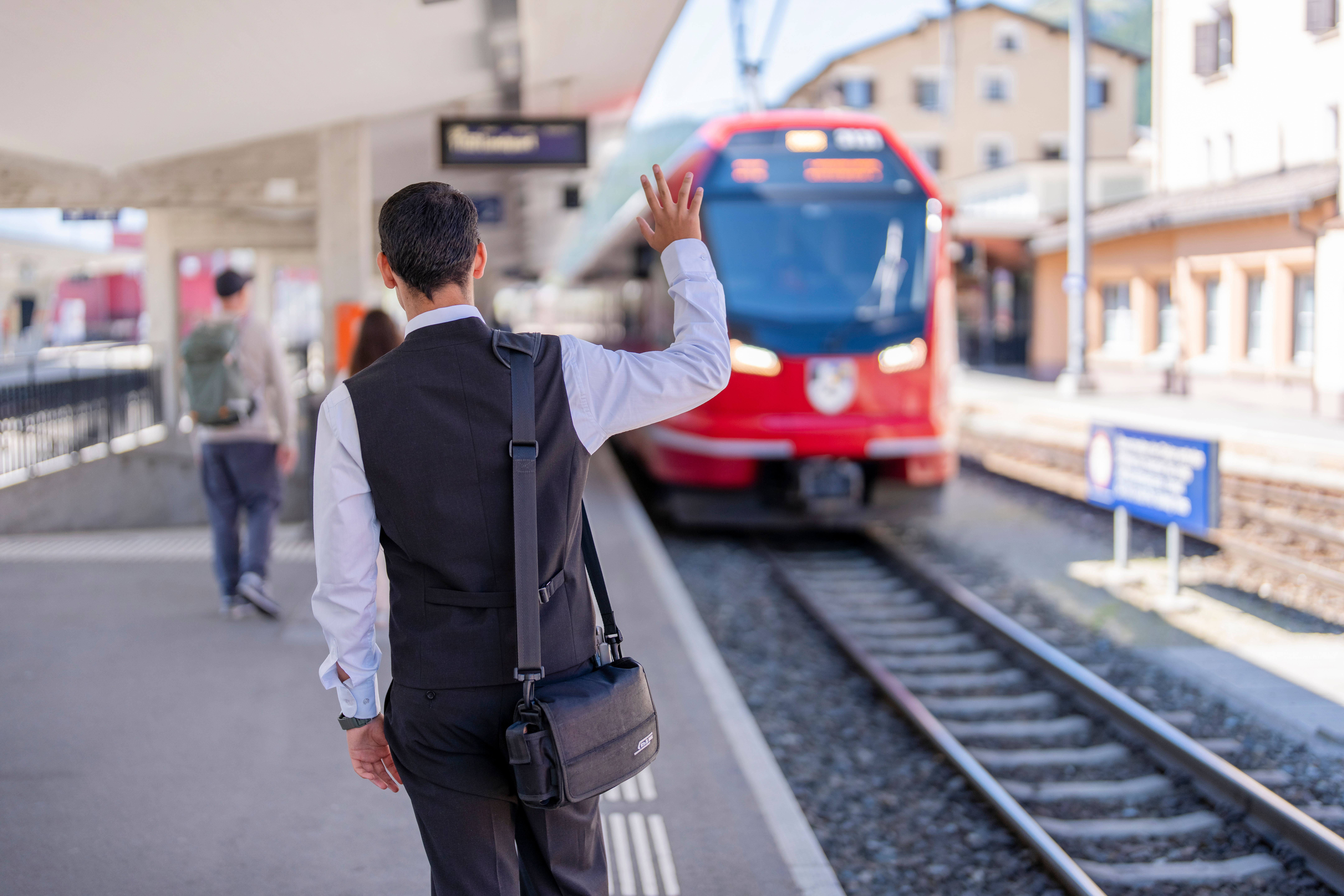 Ein Zugbegleiter der Rhätischen Bahn winkt einem einfahrenden Zug zu
