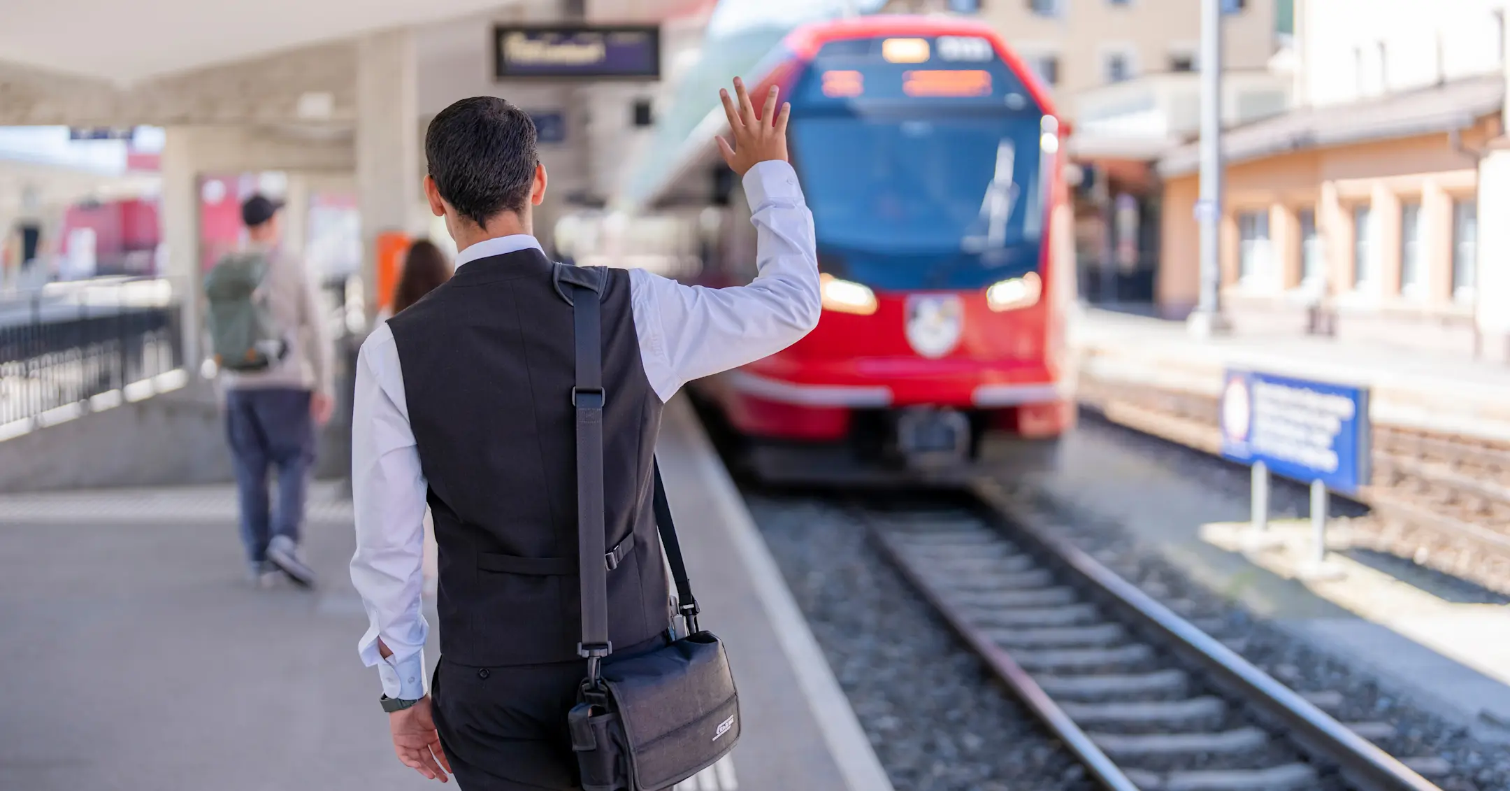 Ein Zugbegleiter der Rhätischen Bahn winkt einem einfahrenden Zug zu
