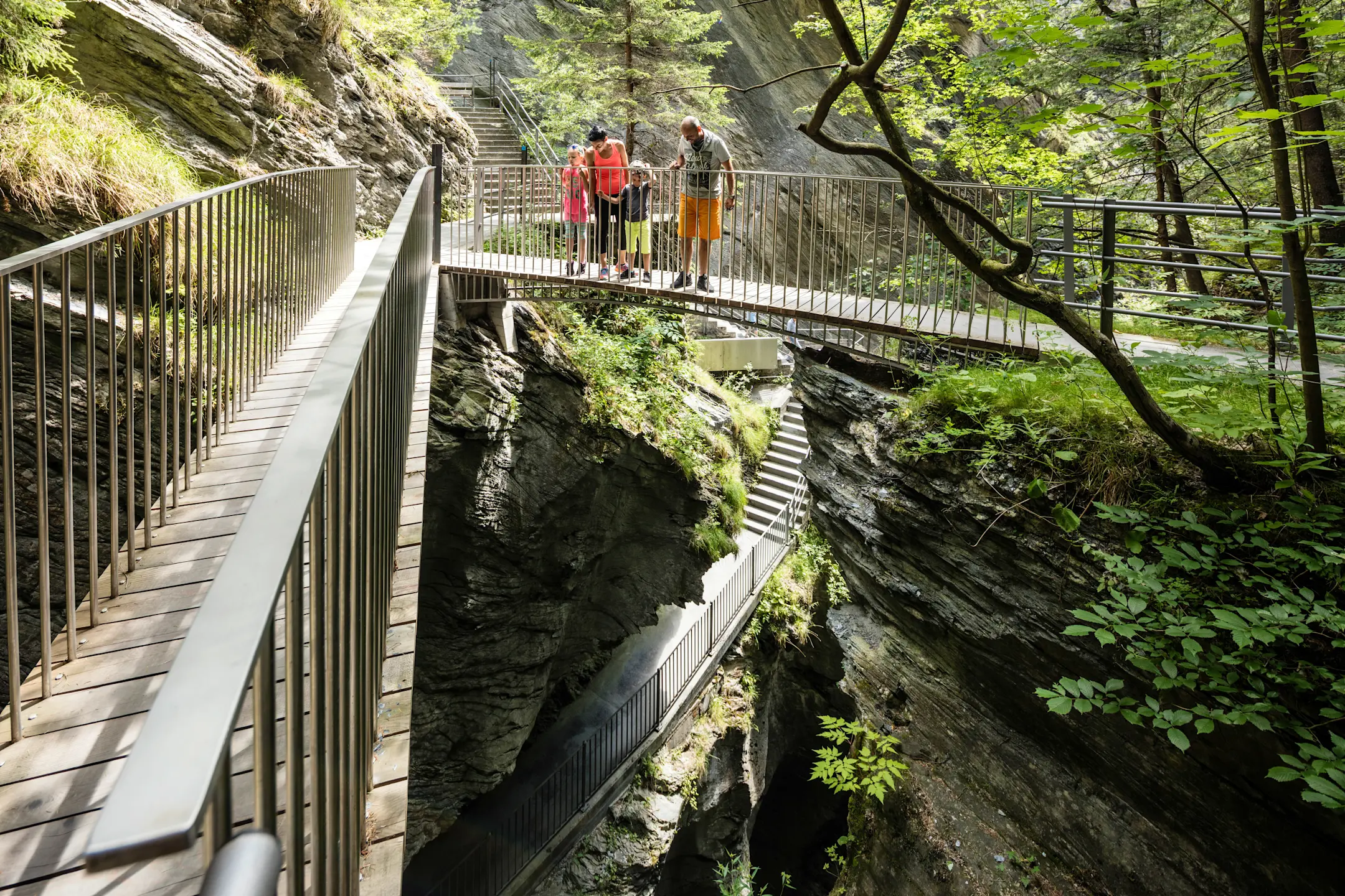 Una famiglia è in piedi sulla scala e osserva le profondità della Gola della Viamala.