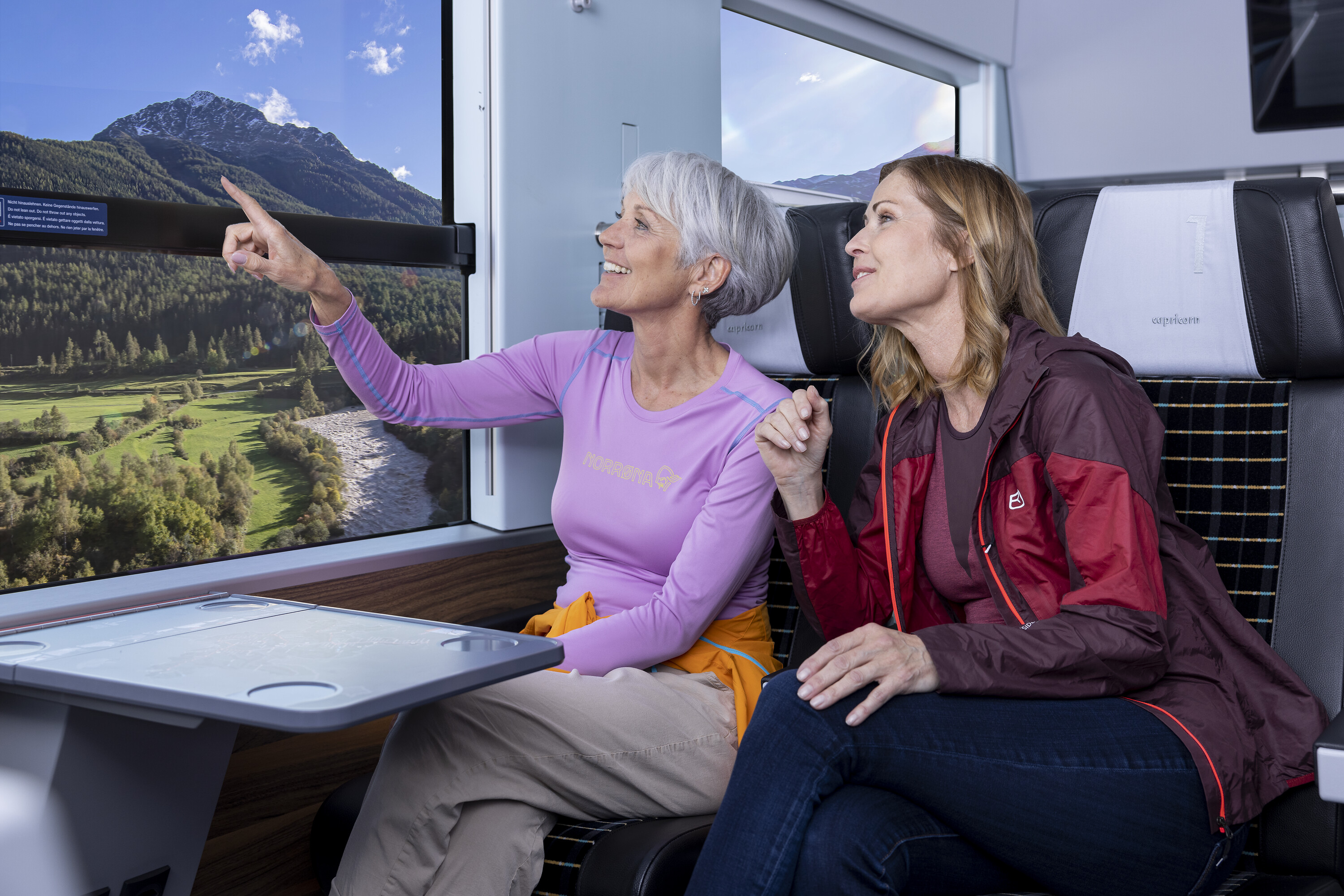 Zwei Frauen in Freizeitbekleidung sitzen im Capricorn-Triebzug und schauen aus dem Fenster.