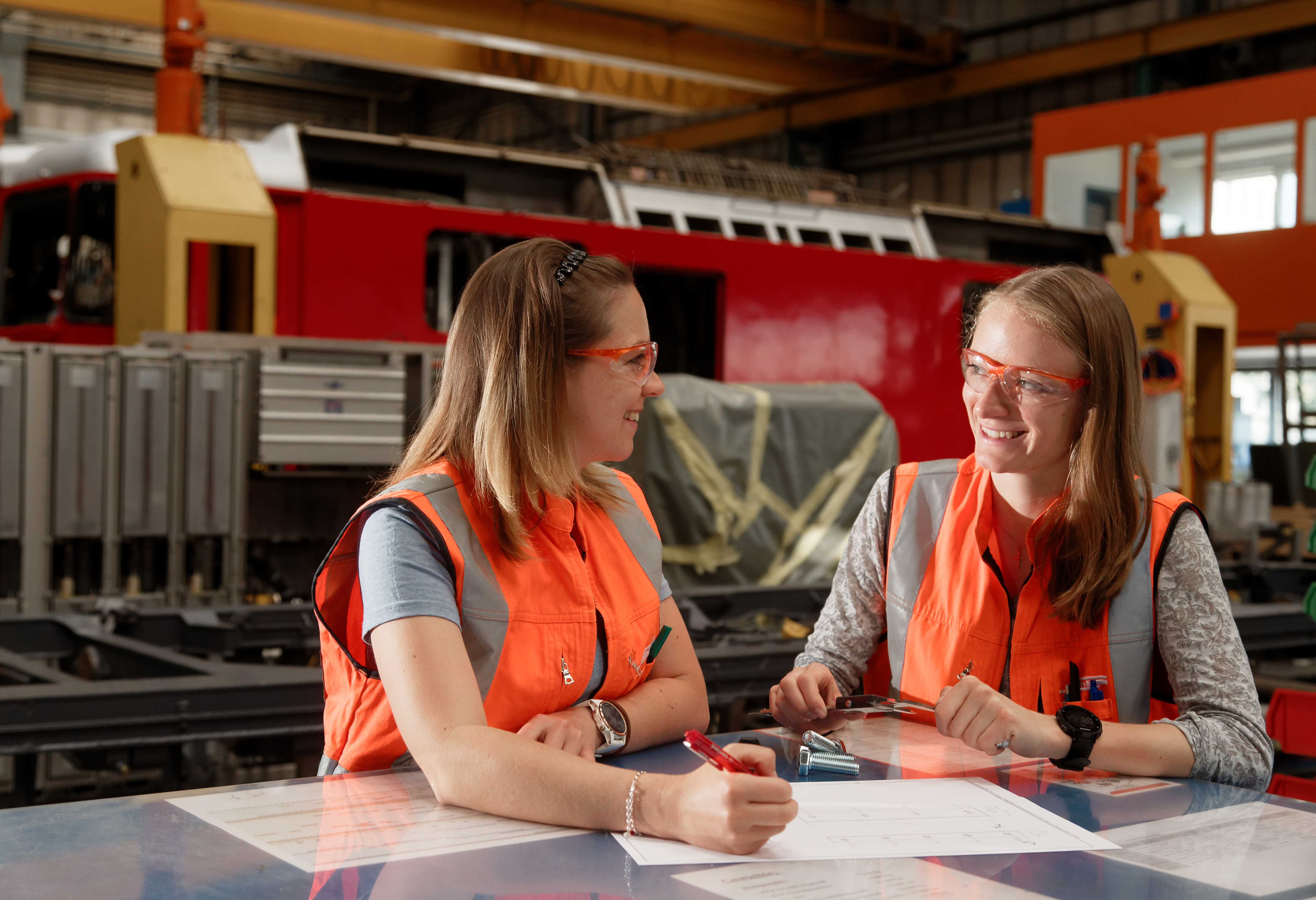 Zwei Konstrukteurinnen der RhB an einem Konstruktionstisch in der Werkstatt vor einem Waggon.