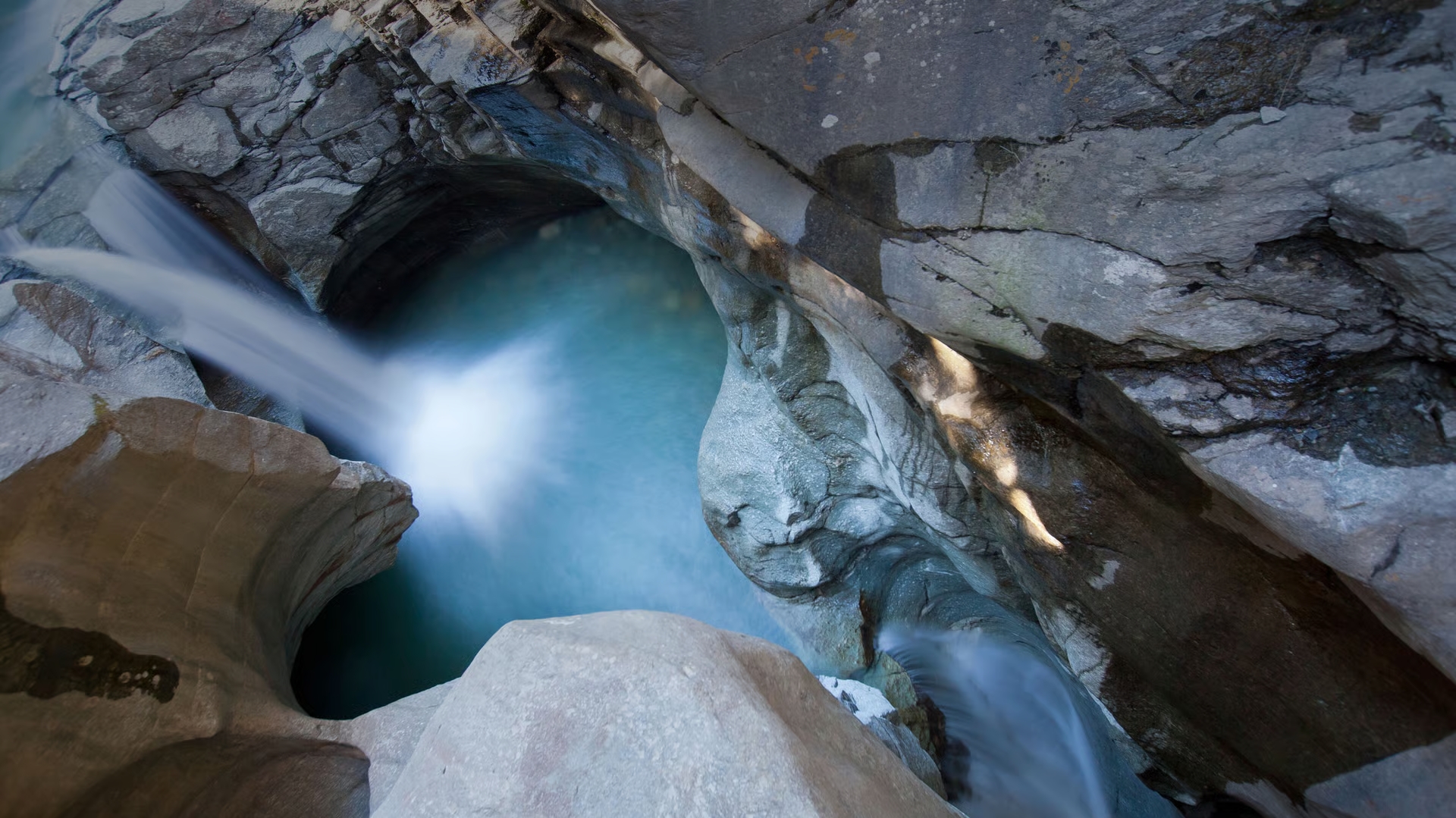 View the glacier mills from above in the Cavaglia Glacier Garden with turquoise water and smoothly polished rock.