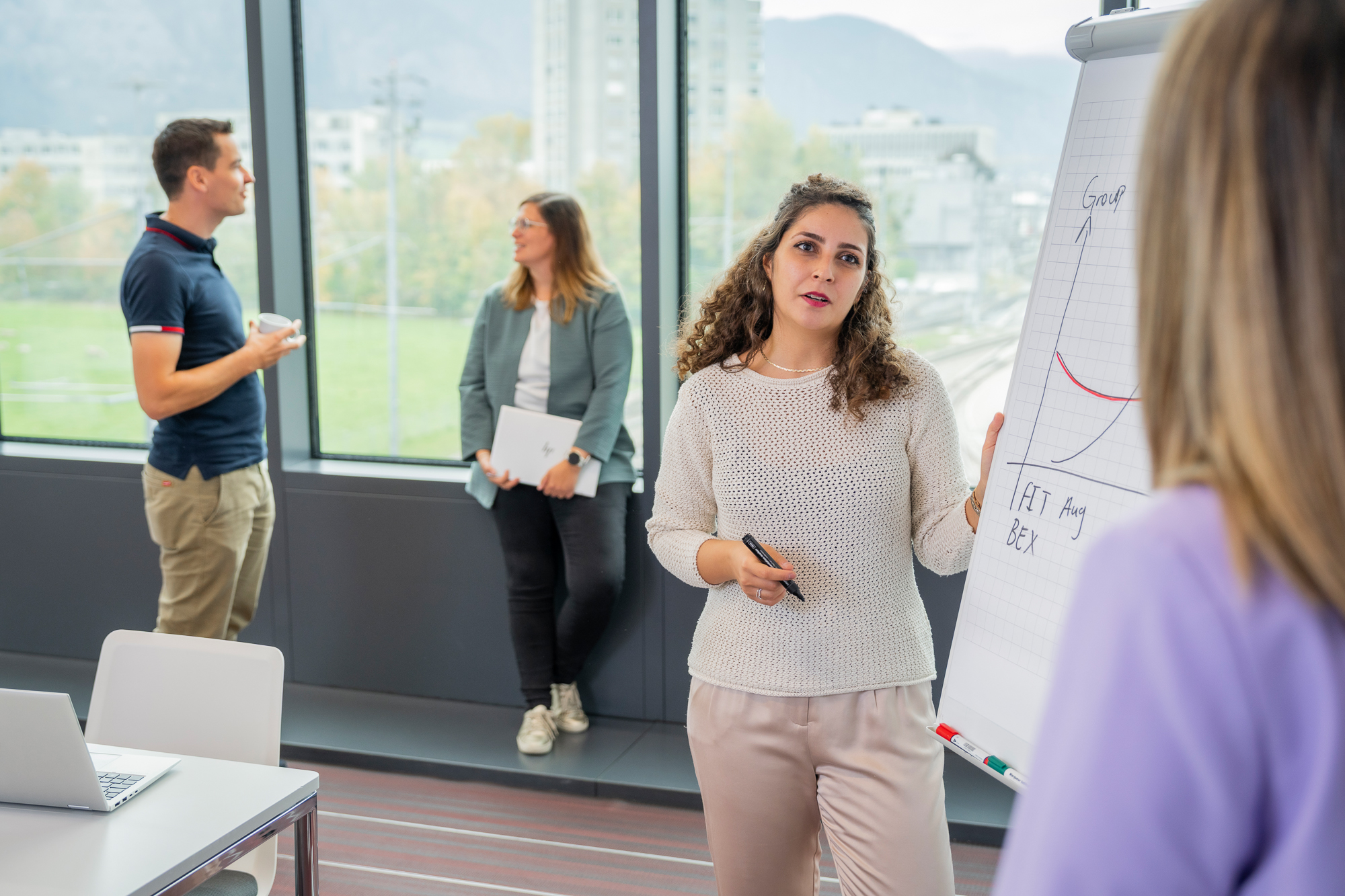 Eine RhB Mitarbeitende erklärt etwas am Flipchart, im Hintergrund 2 Perosnen
