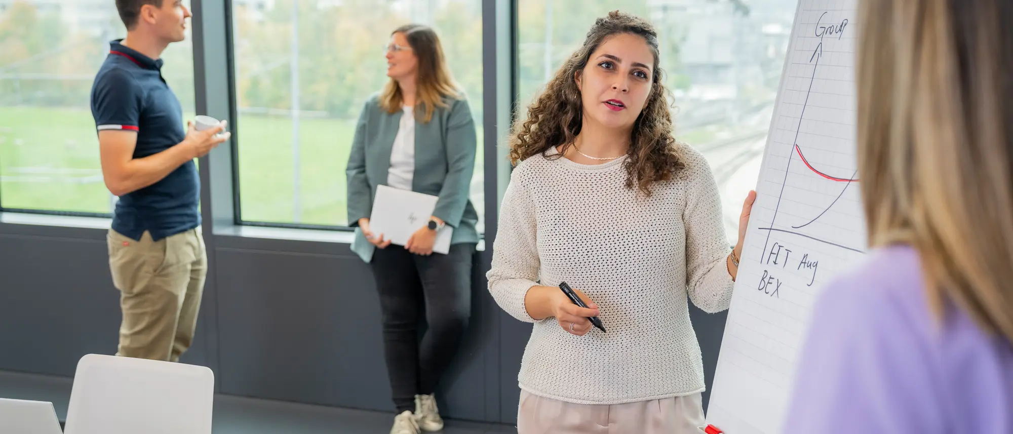 Eine RhB Mitarbeitende erklärt etwas am Flipchart, im Hintergrund 2 Perosnen