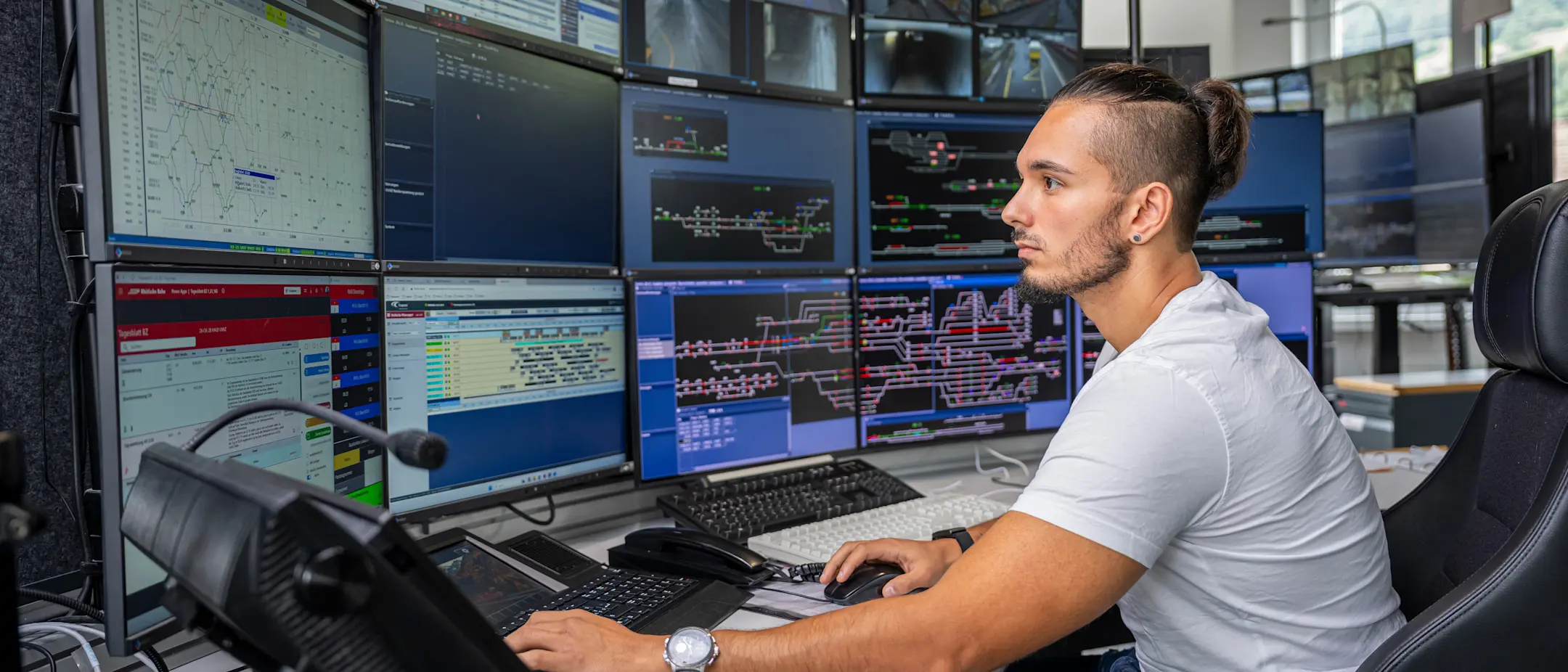 Ein Zugverkehrsleiter sitzt vor zahlreichen Monitoren bei der Arbeit
