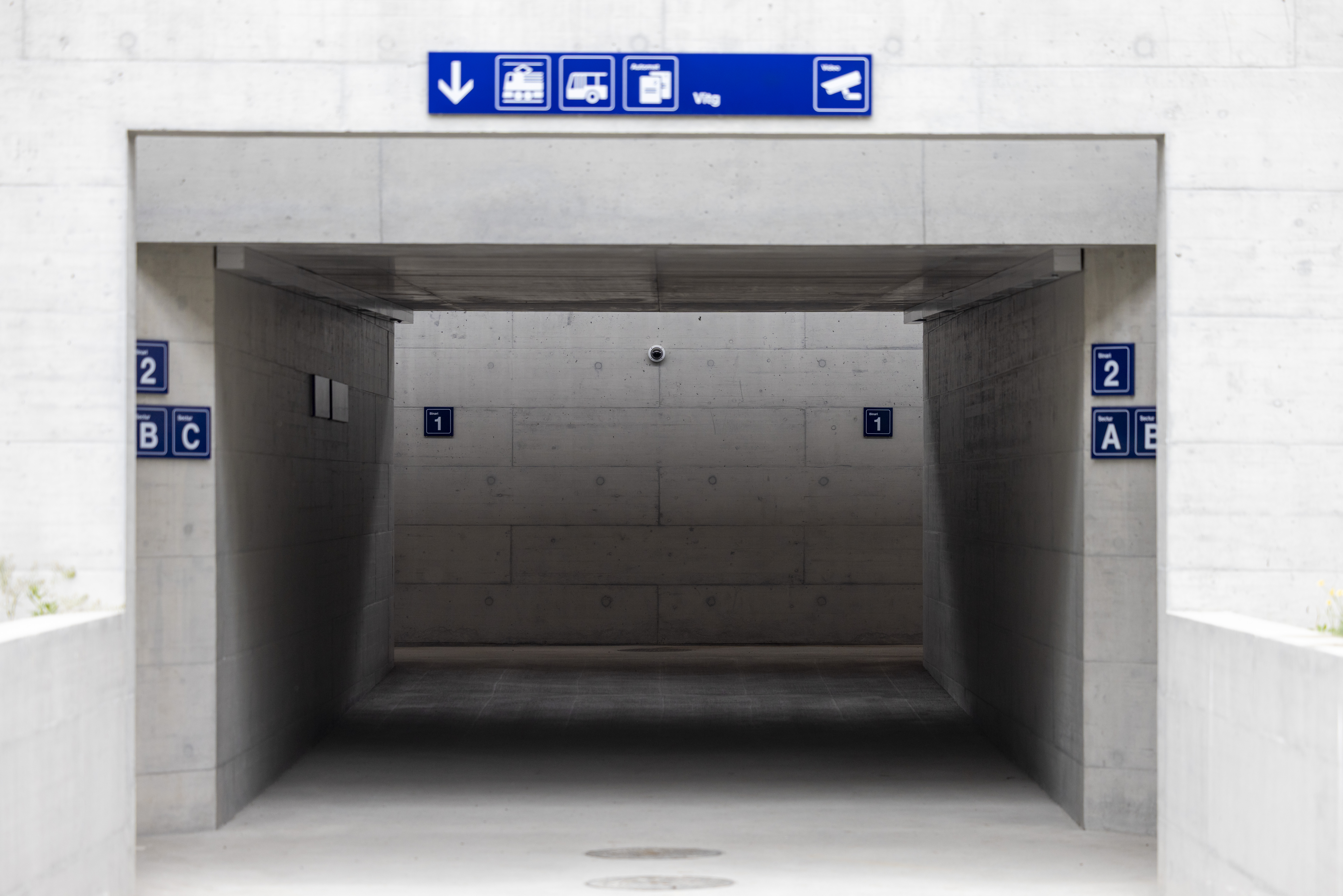 Underpass at Trun railway station with signposts to the tracks, video surveillance and information signs.