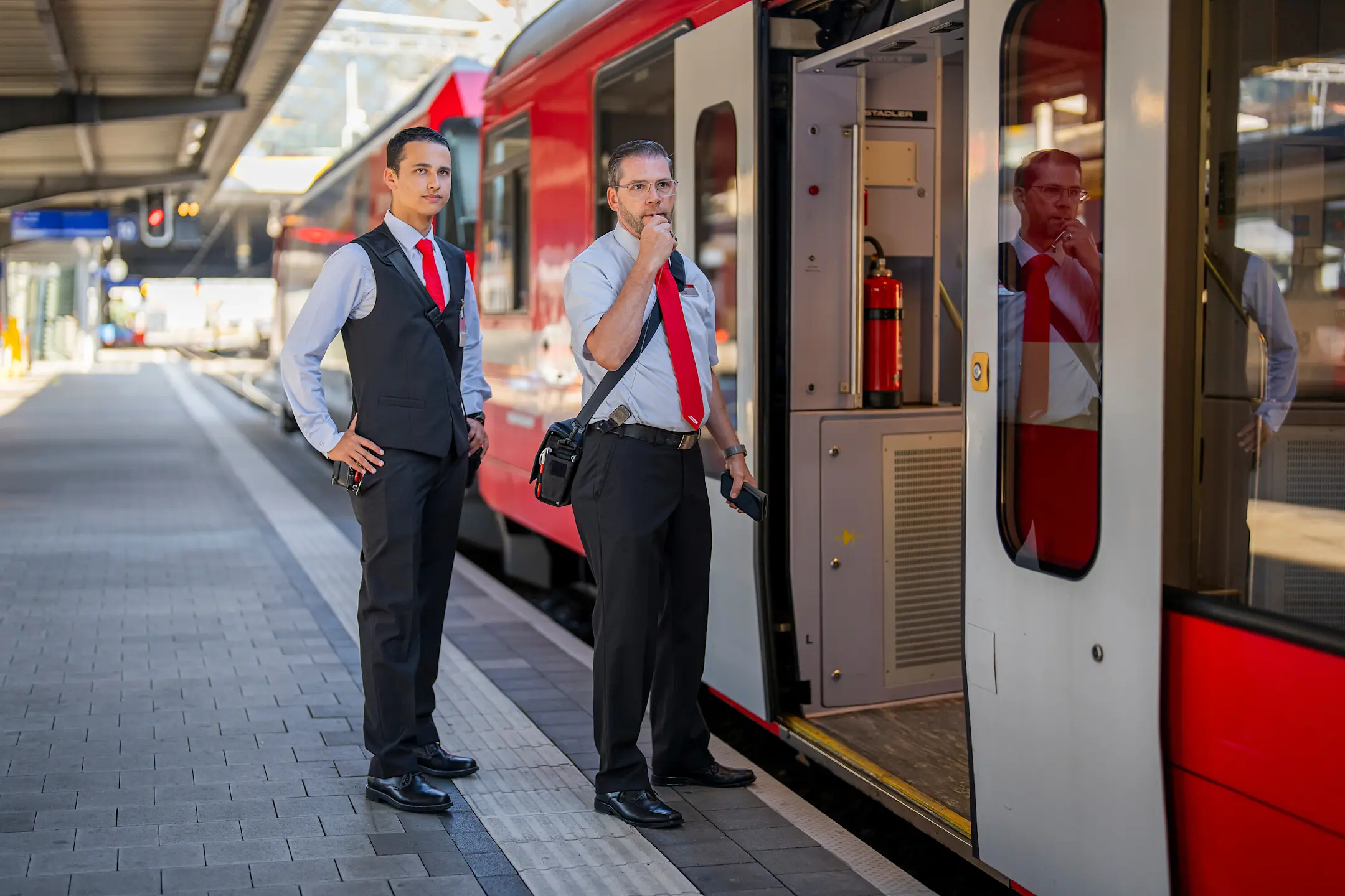 Zwei Zugbegleiter auf dem Bahnsteig kurz vor Abfahrt des Zuges – einer gibt mit seiner Pfeife das Signal.