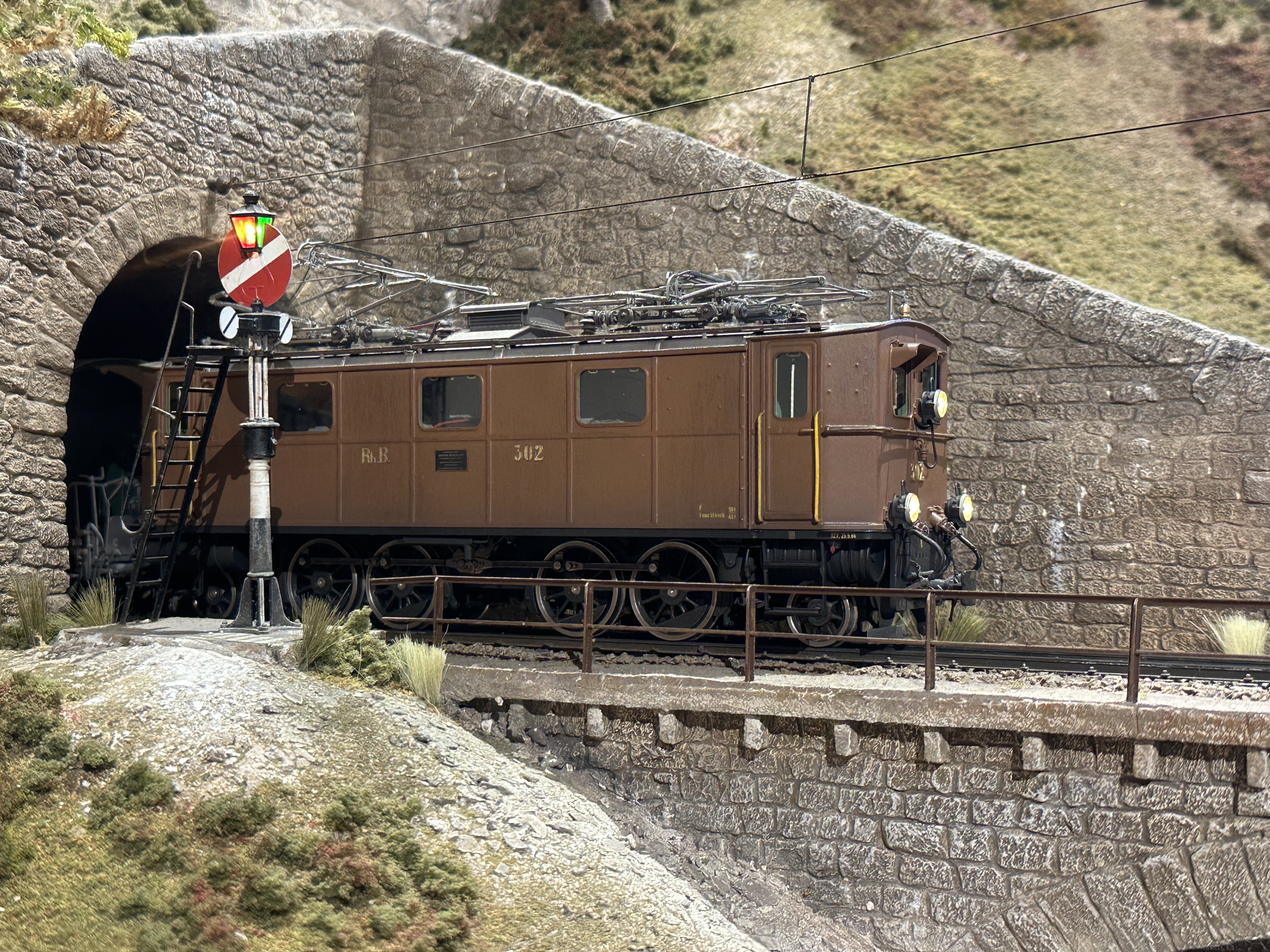 A brown model railway locomotive emerges from the tunnel.