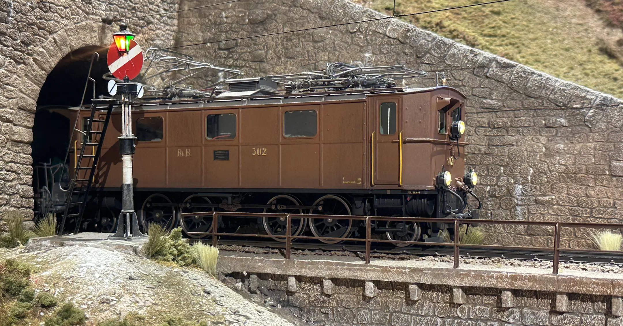 Eine braune Modelleisenbahn-Lok fährt aus dem Tunnel.