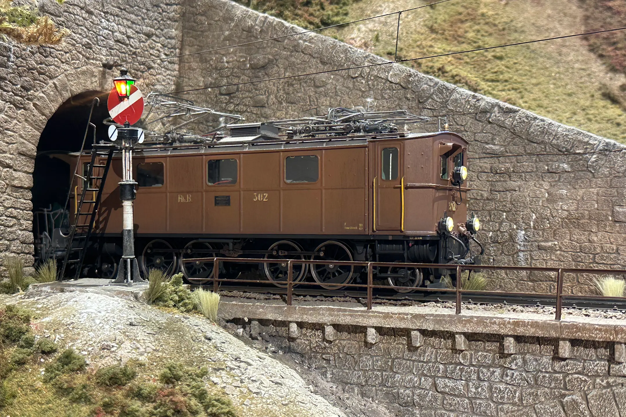 Eine braune Modelleisenbahn-Lok fährt aus dem Tunnel.