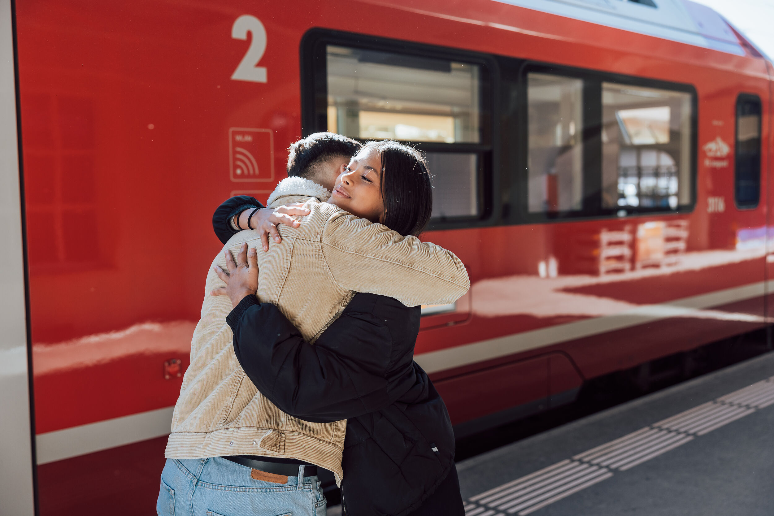 Zwei junge Erwachsene umarmen sich vor dem Zug der Rhätischen Bahn.
