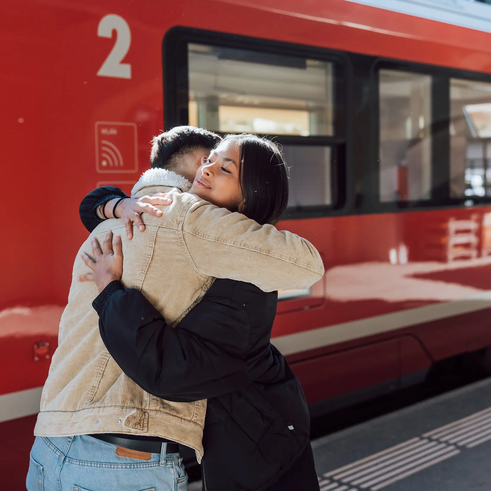 Zwei junge Erwachsene umarmen sich vor dem Zug der Rhätischen Bahn.
