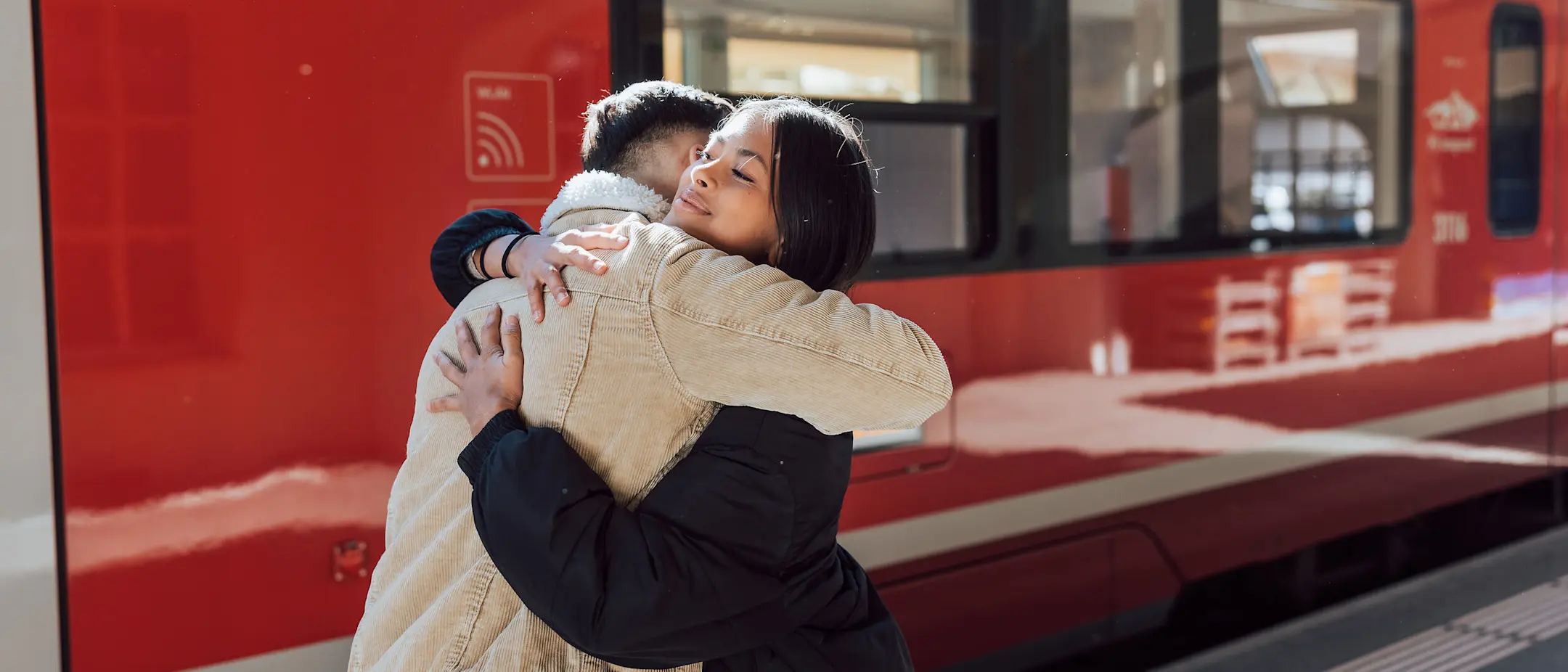 Zwei junge Erwachsene umarmen sich vor dem Zug der Rhätischen Bahn.