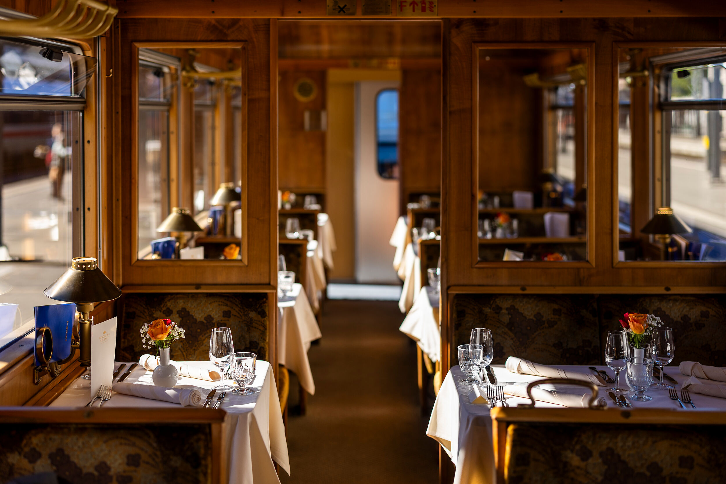 Interno della carrozza ristorante Gourmino con tavoli apparecchiati di bianco.