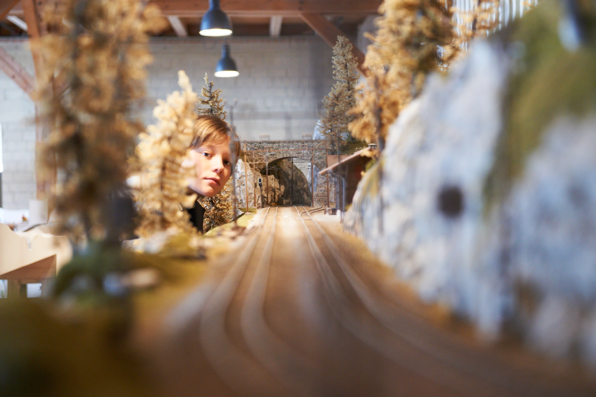 Ein Kind blickt neugierig auf eine Modelleisenbahnanlage mit Gleisen, Tunneln und Miniaturbäumen im Bahnmuseum Albula.