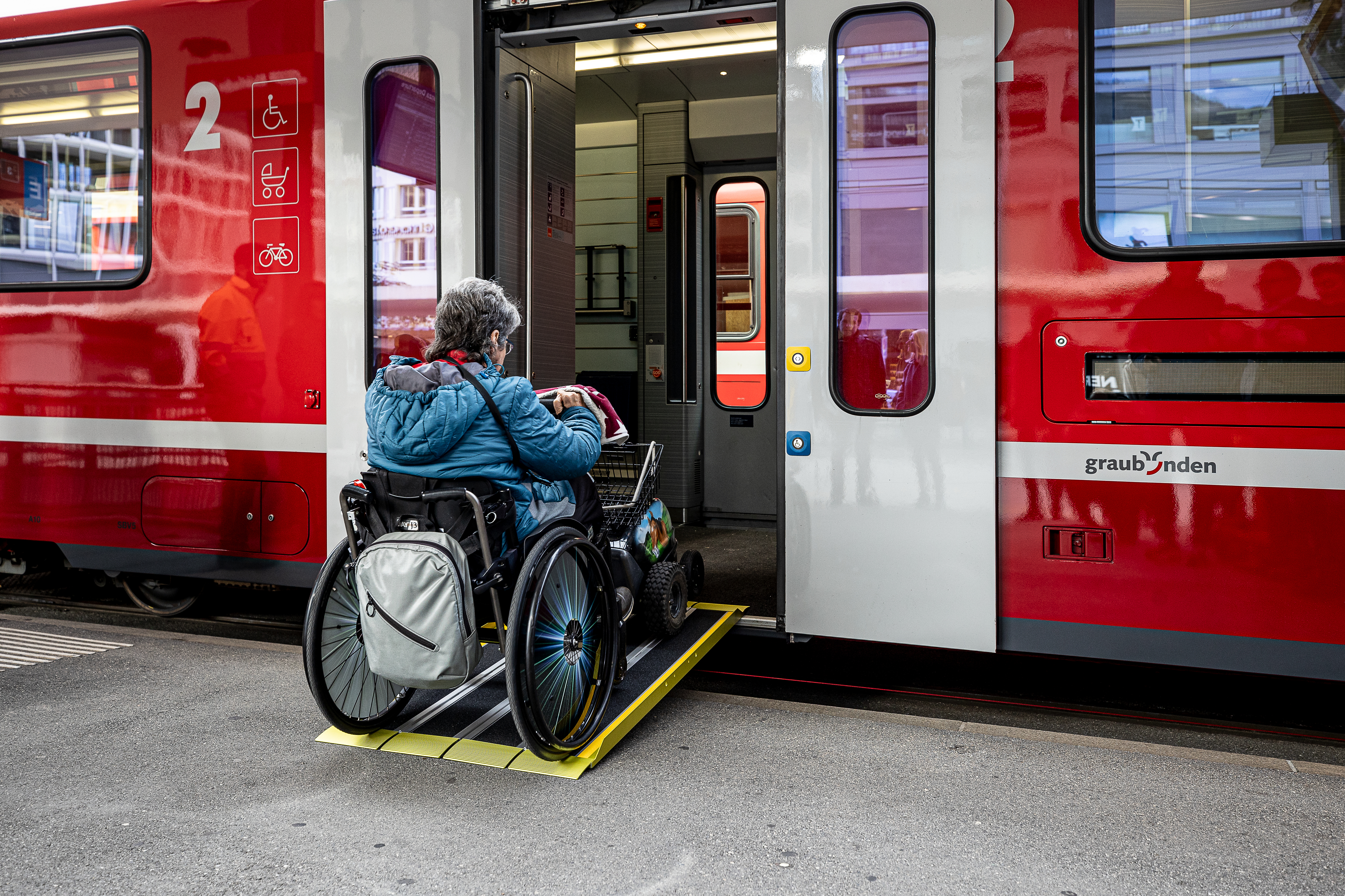 Eine Rollstuhlfahrerin fährt über eine Rampe in einen Zug der Rhätischen Bahn.