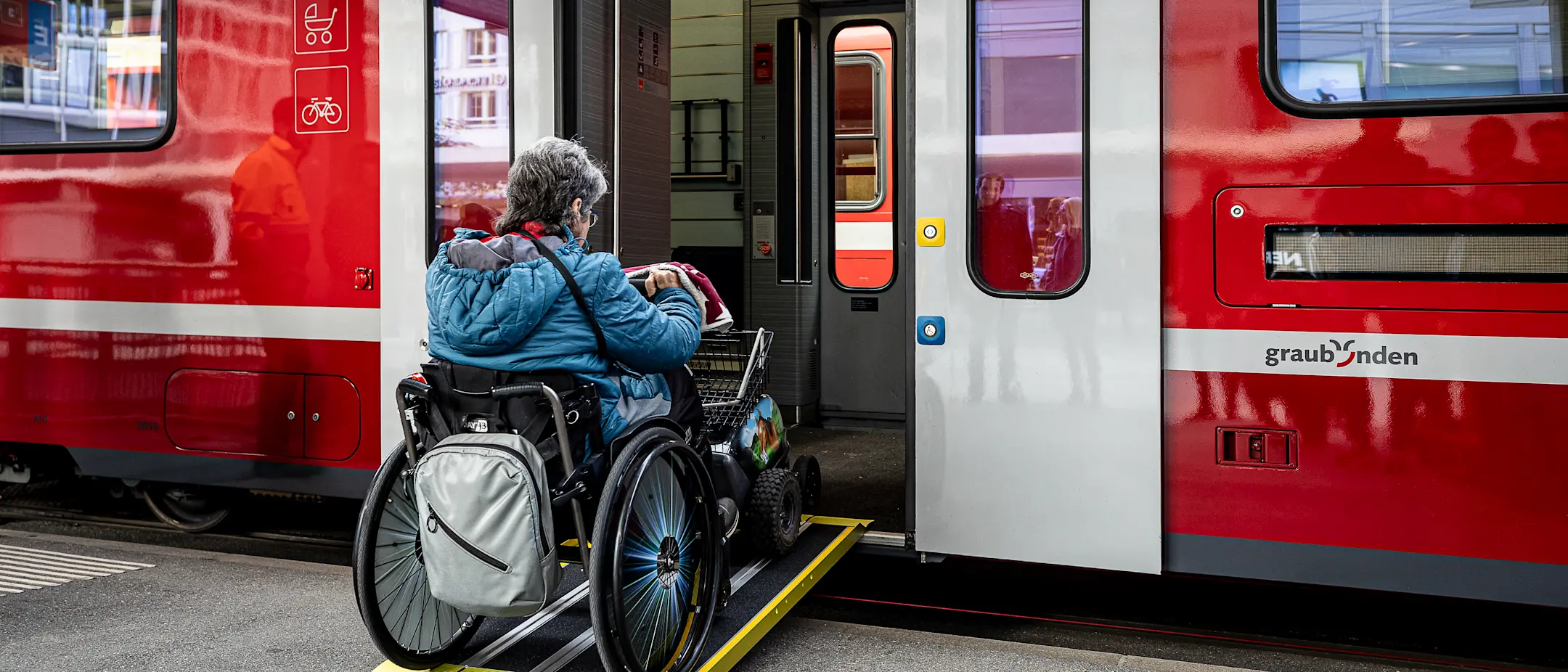 Eine Rollstuhlfahrerin fährt über eine Rampe in einen Zug der Rhätischen Bahn.