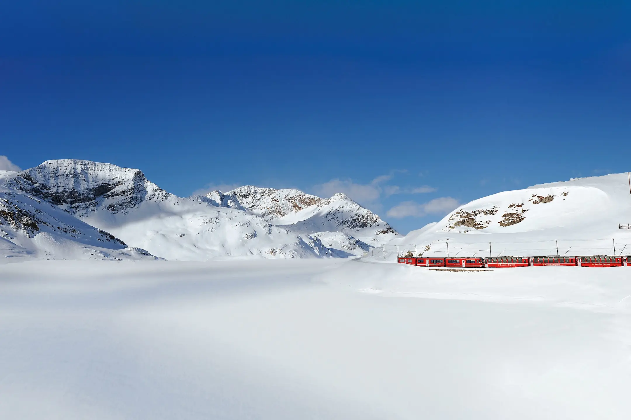 Der Bernina Express fährt durch die verschneite Winterlandschaft am Lago Bianco entlang.