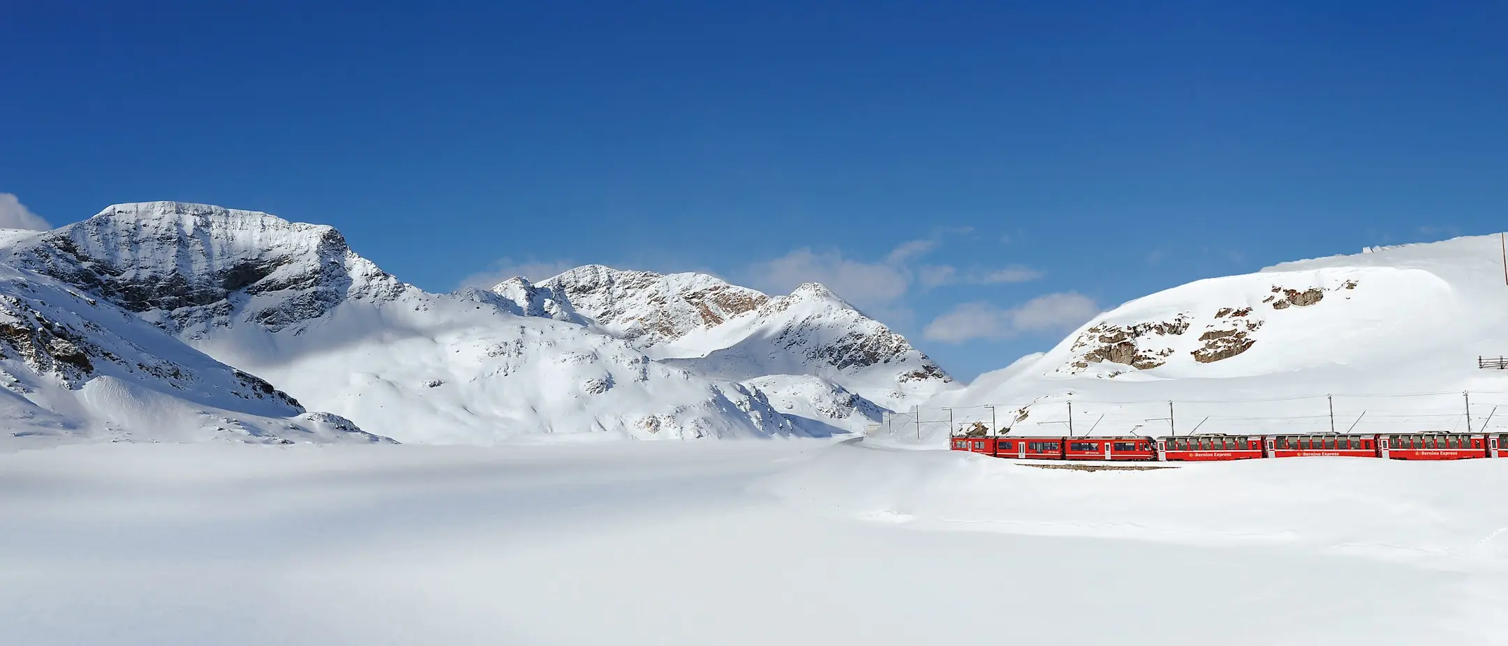 Der Bernina Express fährt durch die verschneite Winterlandschaft am Lago Bianco entlang.