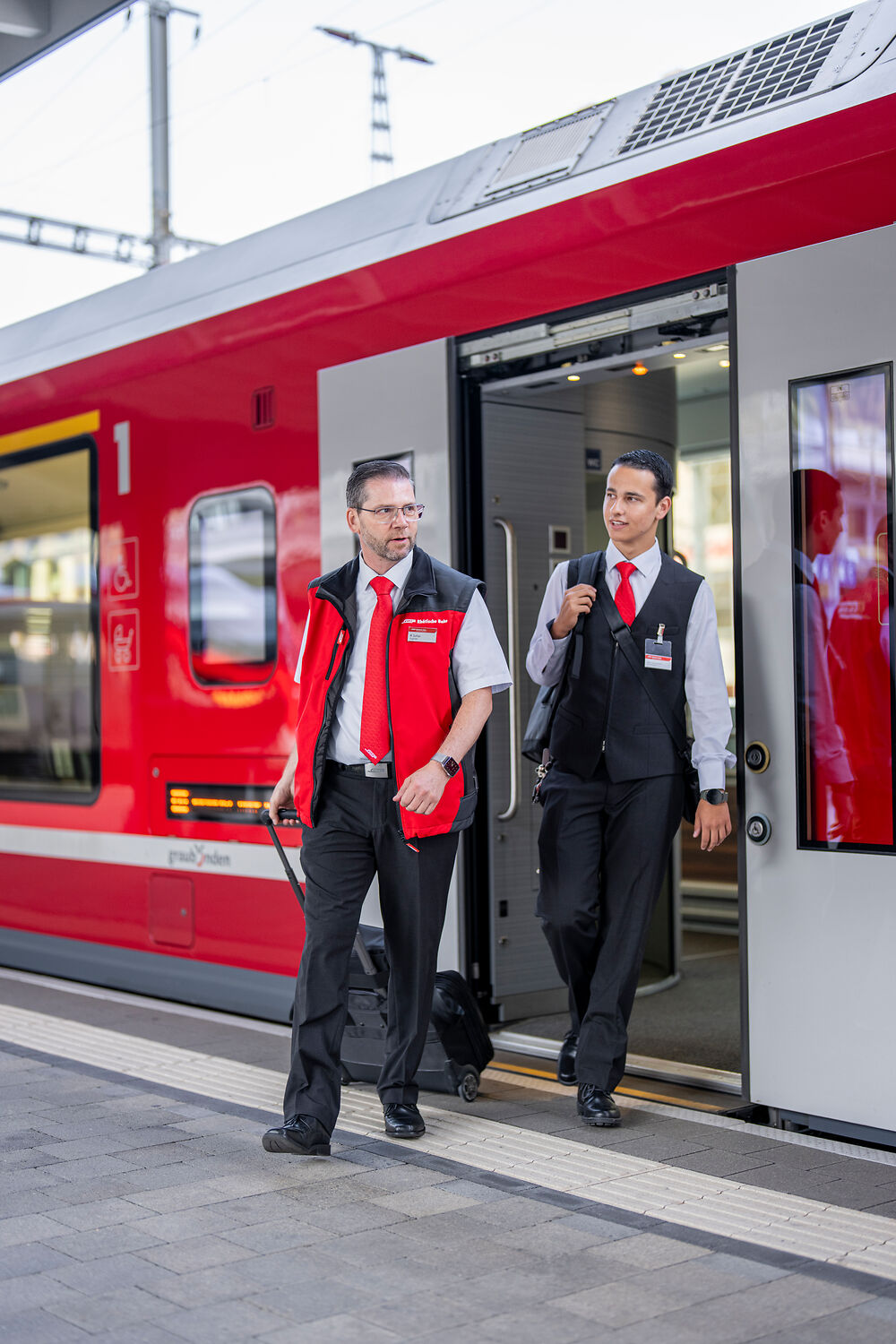 Two train attendants get off a train.