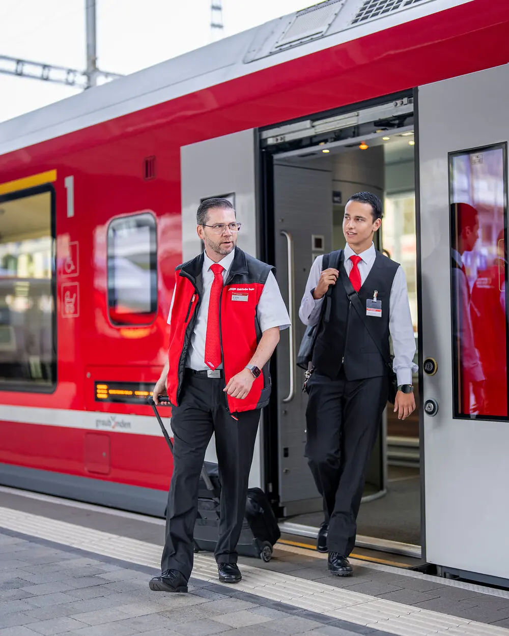 Two train attendants get off a train.