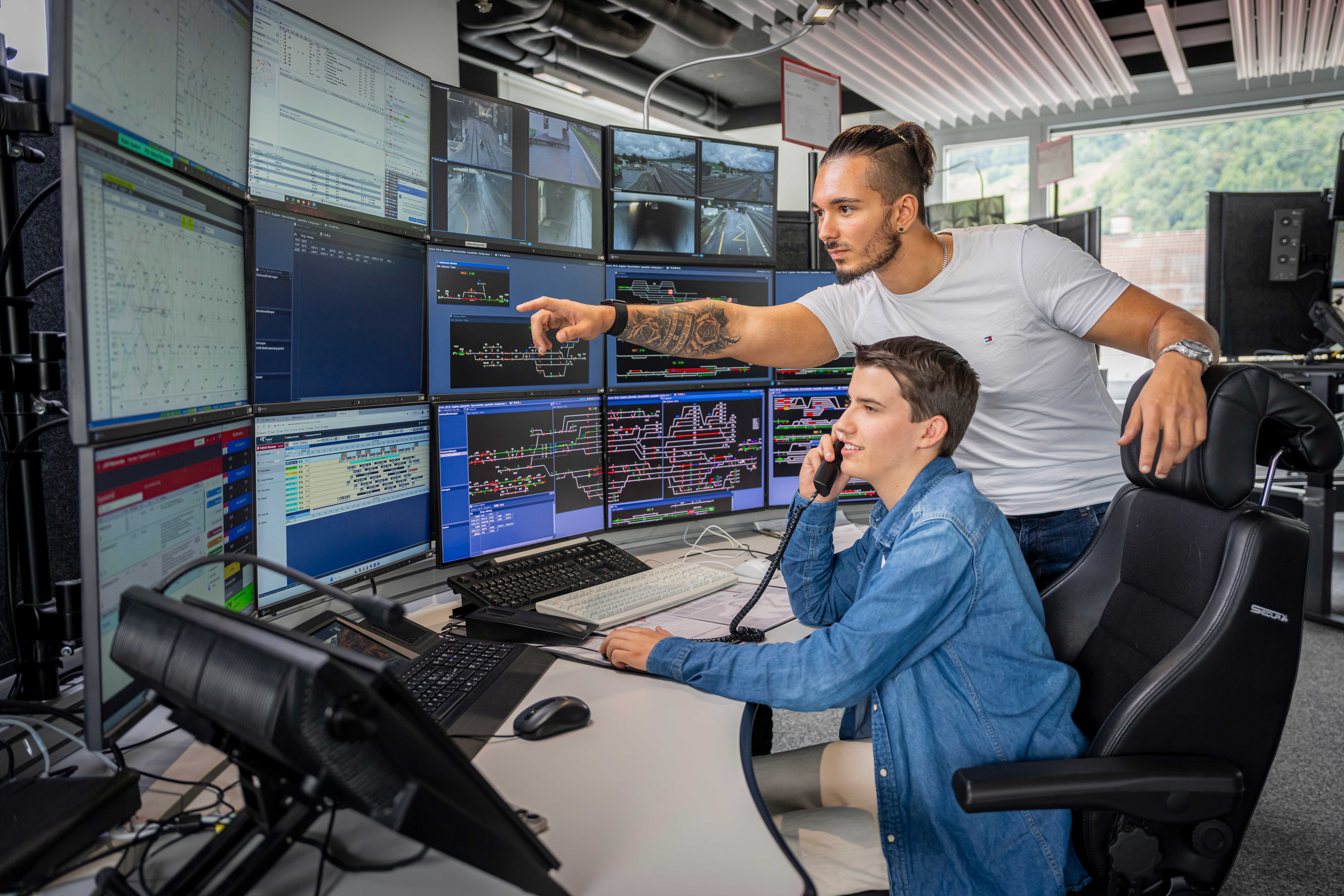 Zugverkehrsleiter erklärt einem Lernenden, der telefoniert