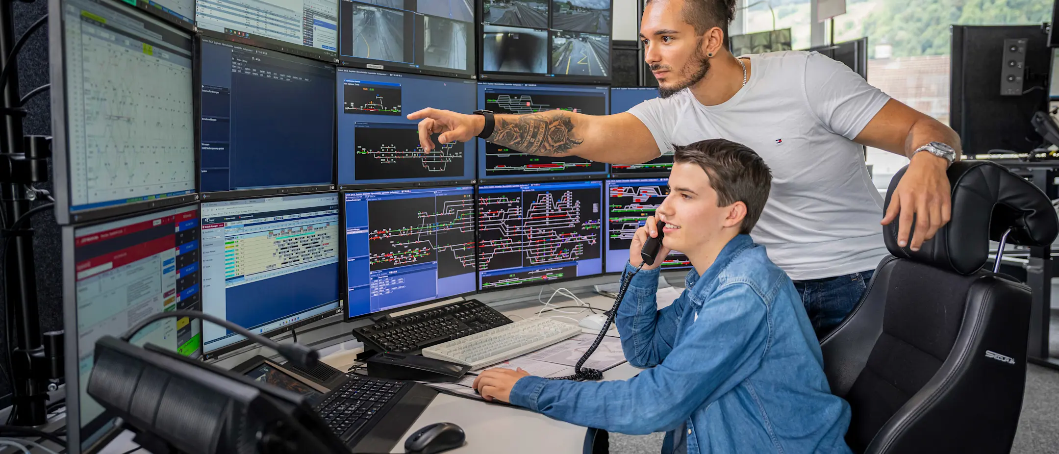 Zugverkehrsleiter erklärt einem Lernenden, der telefoniert
