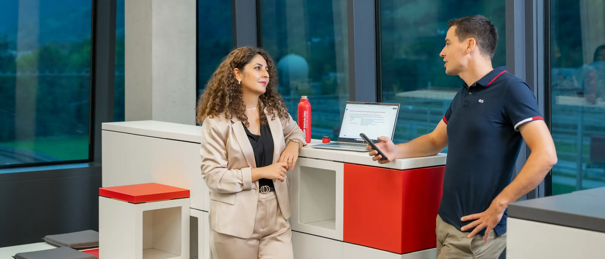 Mitarbeiterin und Mitarbeiter in einer Besprechung, hinten ein Laptop