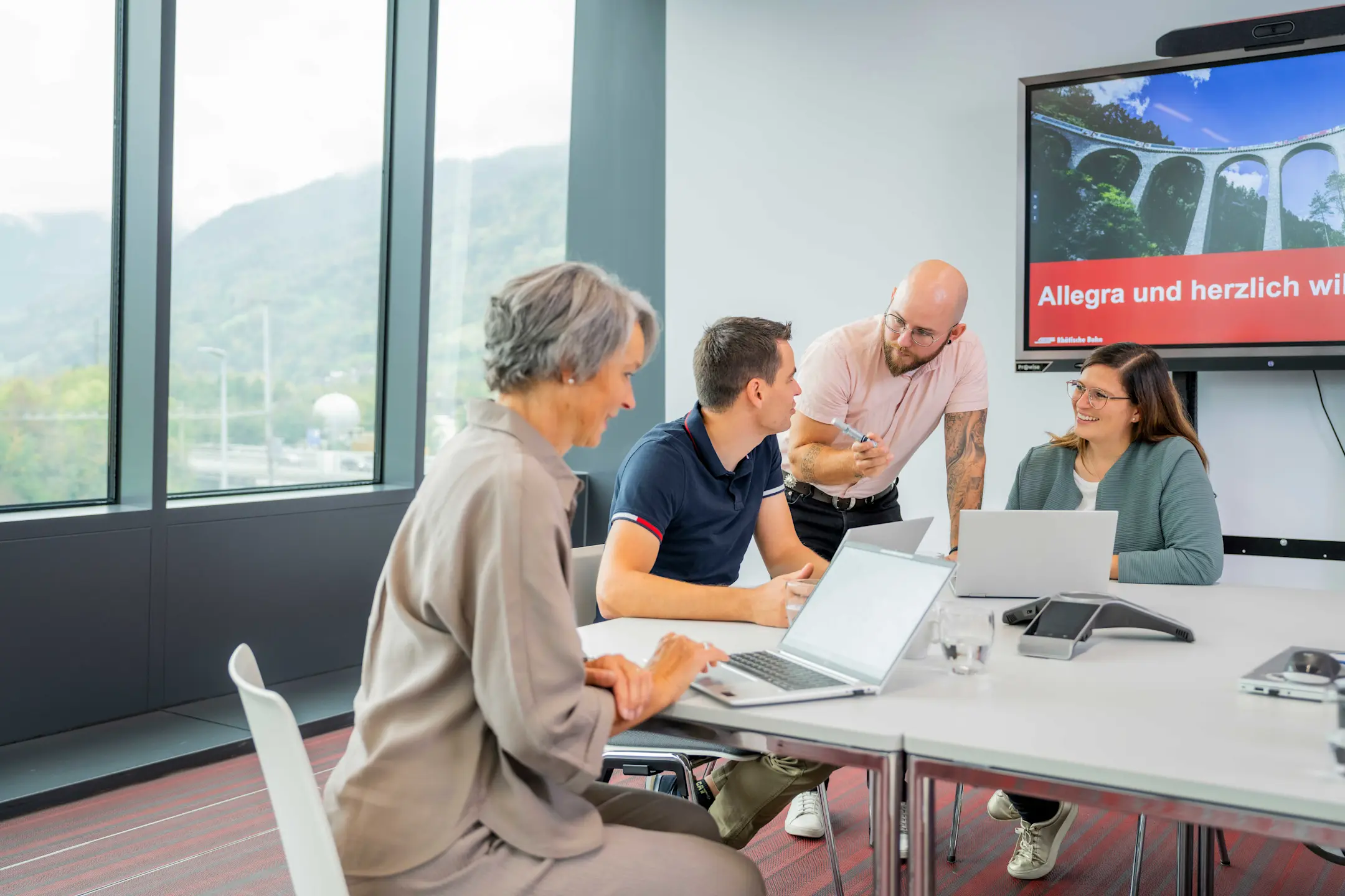 4 Mitarbeitende an einem Tisch bei einer Besprechung mit Notebooks