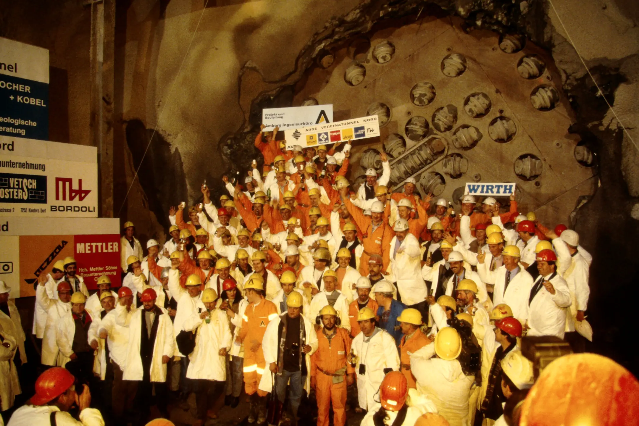 Mitarbeitende der Baufirmen feiern vor dem Bohrkopf der Tunnelbohrmaschine am 26. März 1997 den Durchschlag am Vereinatunnel