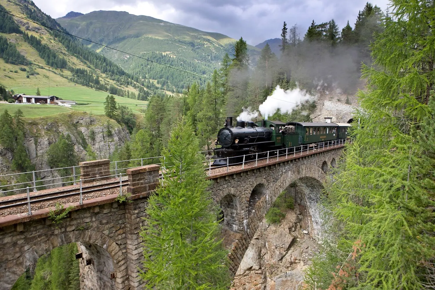 Historischer Dampfzug der Rhätischen Bahn auf dem Viadukt bei Cinuos-chel Brail, eingebettet in die Landschaft des Engadins.