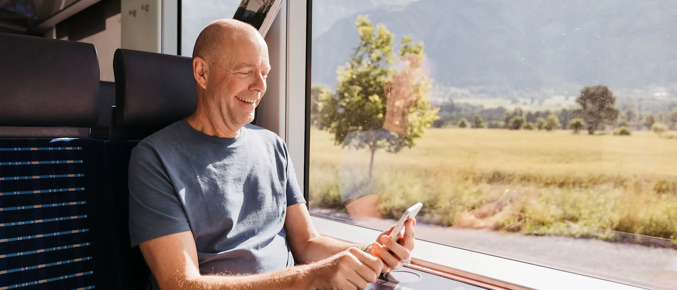 Ein Mann sitzt im Regiozug der RhB und schaut lächelnd auf sein Smartphone.
